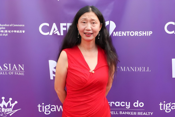Person in a red dress standing in front of a purple backdrop with various logos. The backdrop includes text such as "CAFÉ," "MENTORSHIP," and "Hall of Fame."