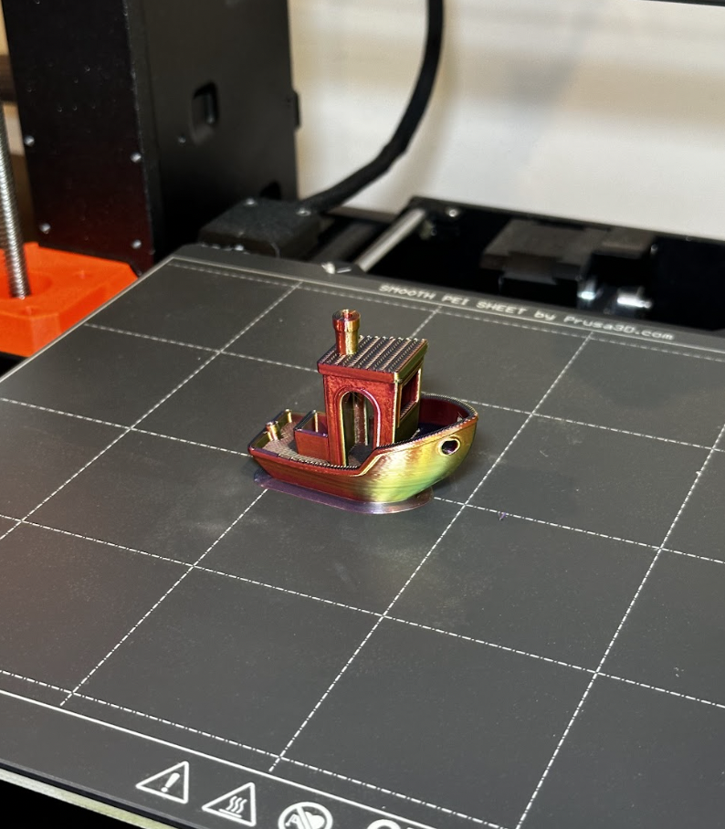 A colorful 3D-printed boat model on a 3D printer bed with grid lines.