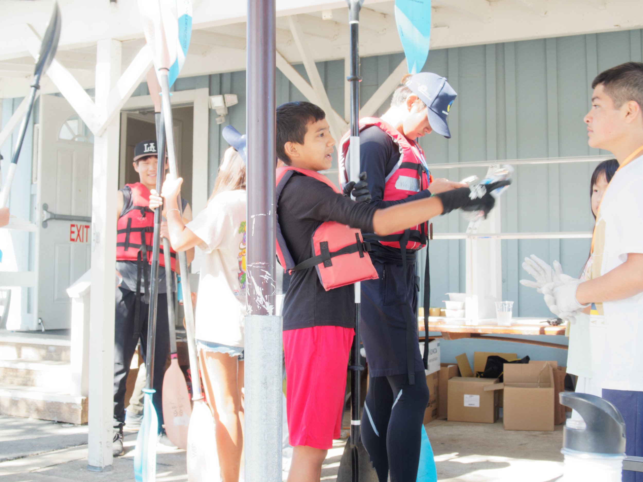Group of people wearing life vests preparing for kayaking with paddles.