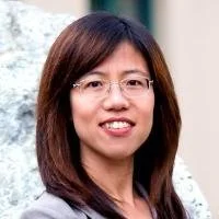 Headshot of a woman with shoulder-length dark hair, glasses, and a smile, indoors with a neutral background.