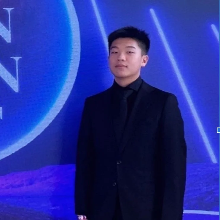 Person in a black suit standing against a blue background with lighting effects.