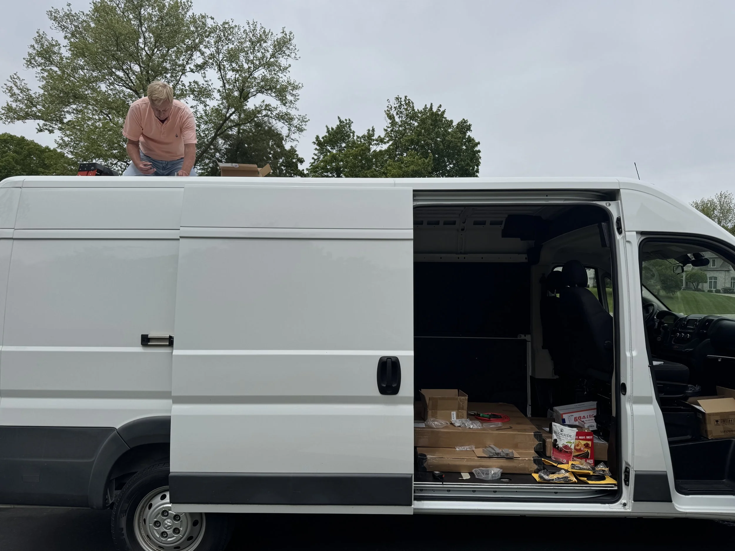 A man works from the top of a white van, adding bolts in a custom van home build