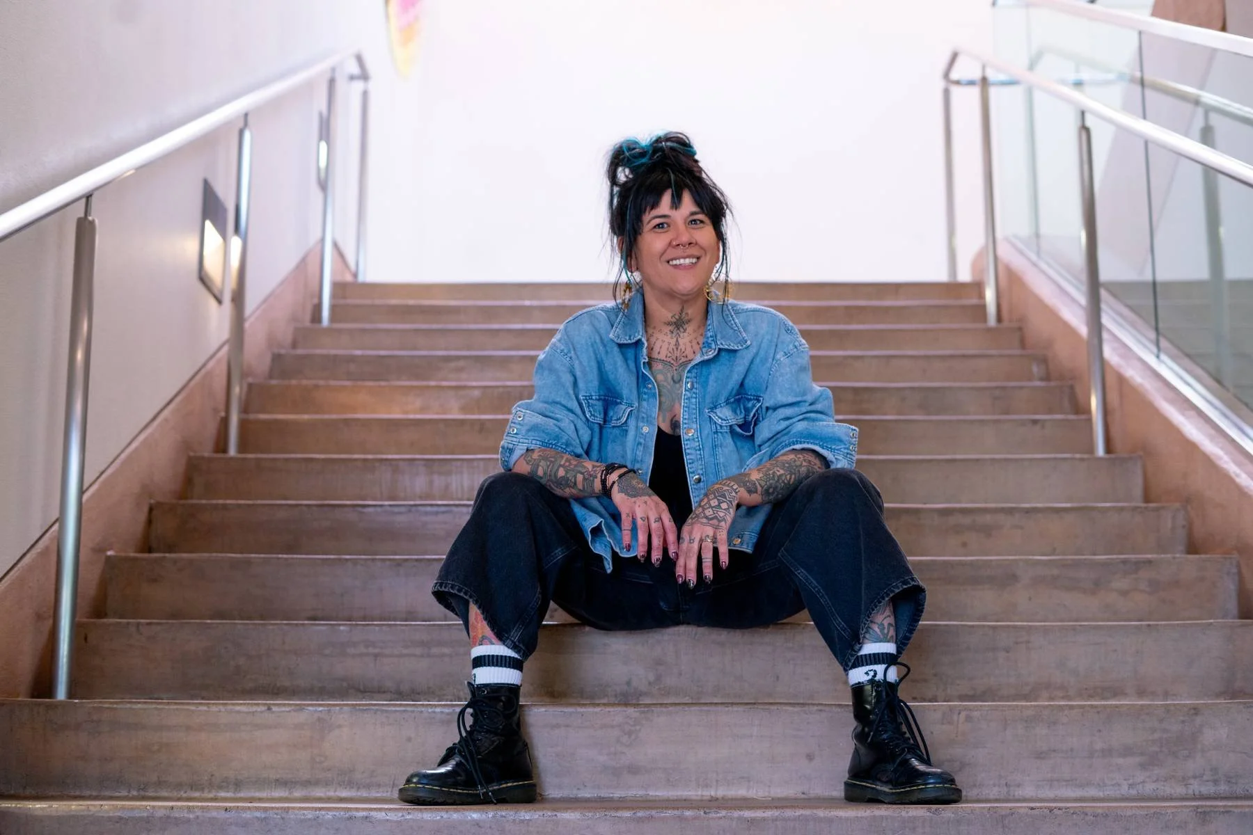Woman with a jean jacket and boots sitting on a staircase.