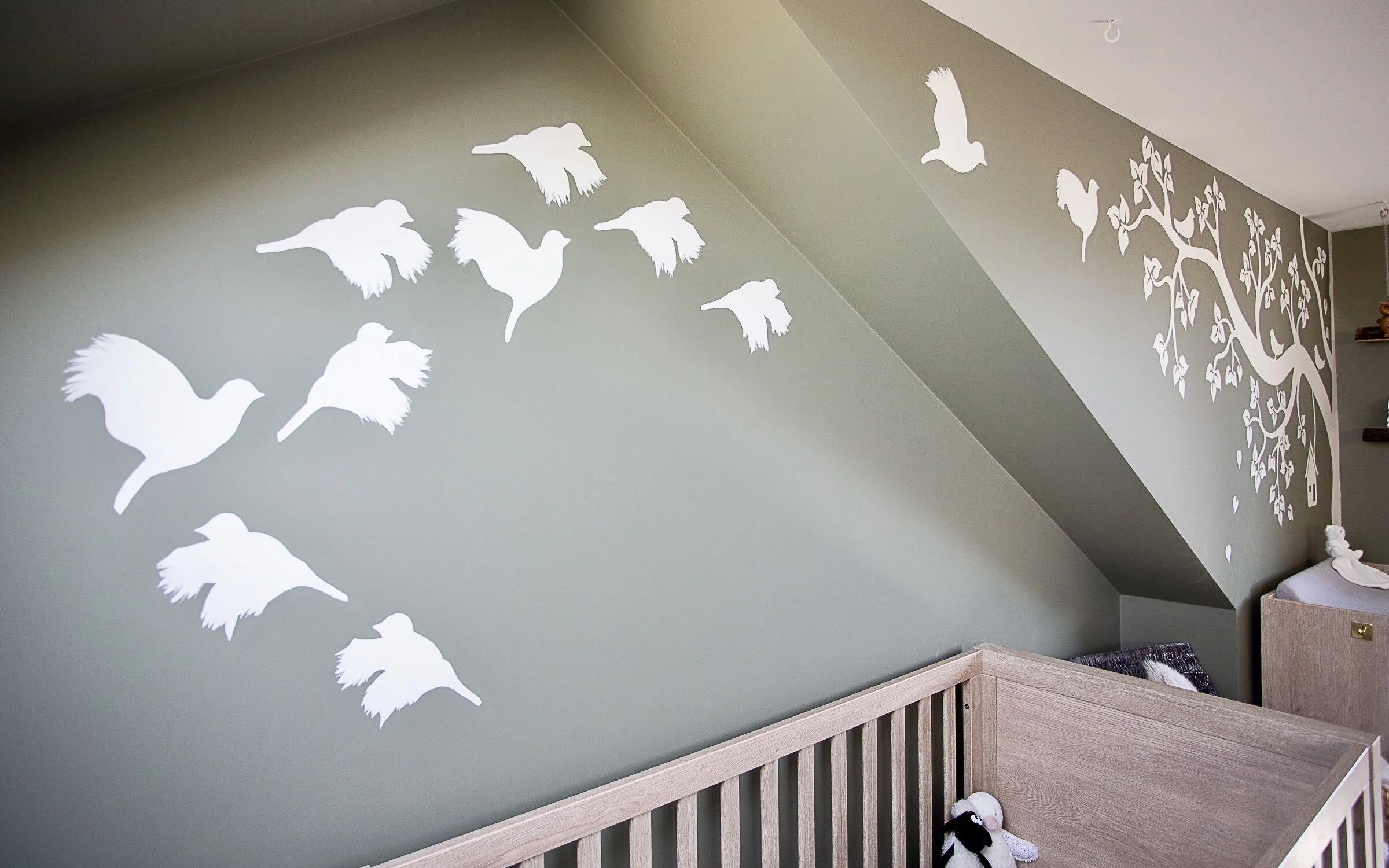 A closeup of the birds on the mural, which are flying toward the autumnal tree.The mural is green, with designs in a pink and off-white colour combination. 