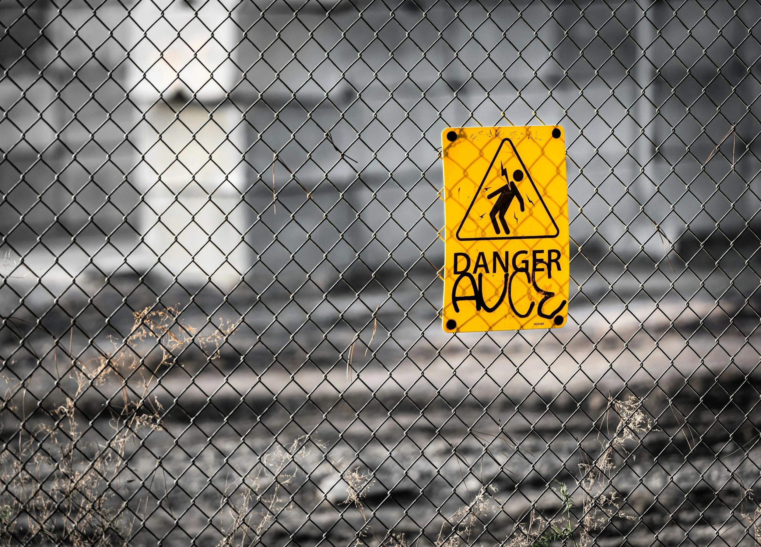 Yellow danger sign with an electric shock symbol on a chain-link fence.