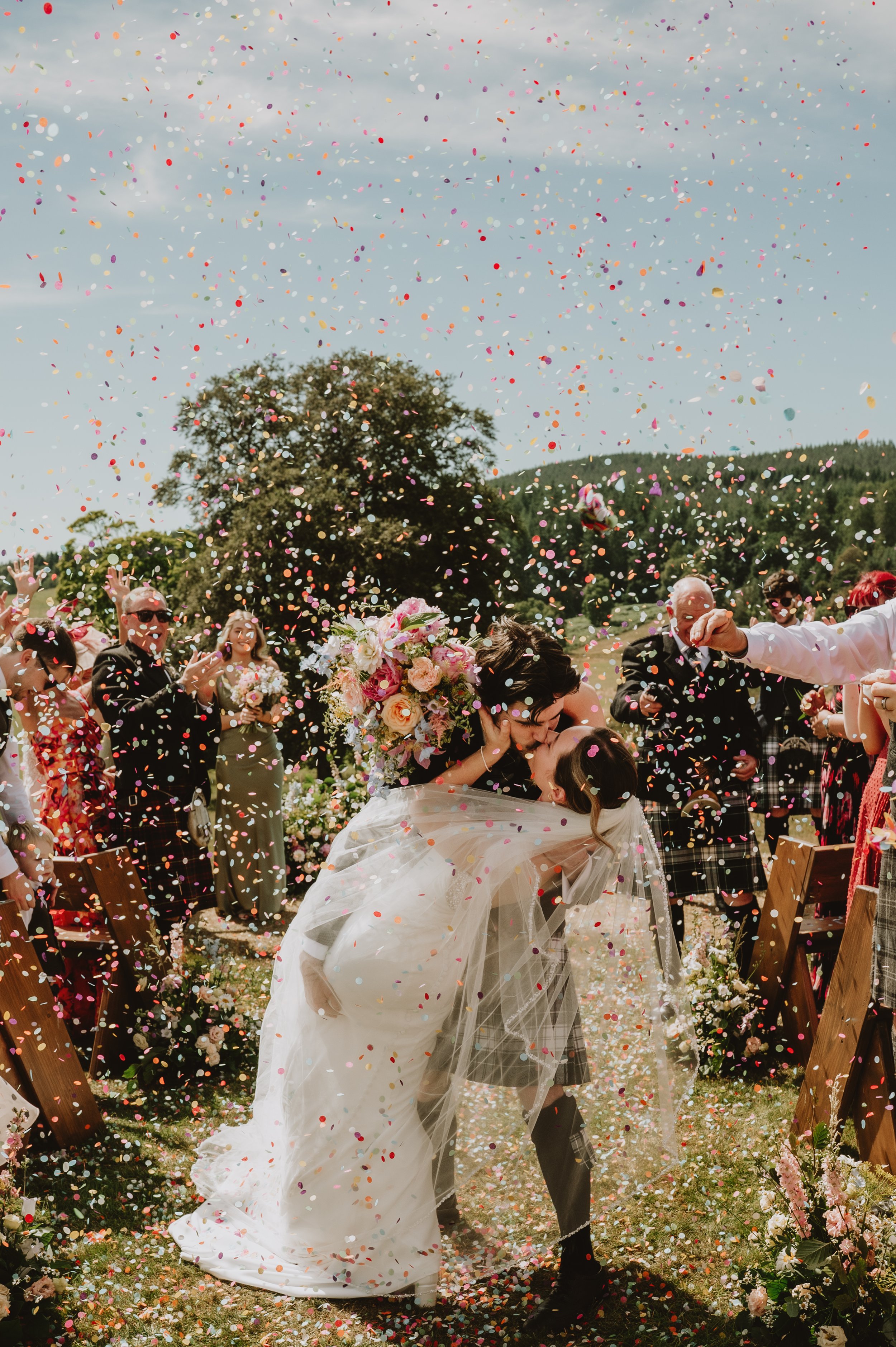 Bride and groom kiss during confetti walk n their wedding day, captured by Jules Williams Photographer