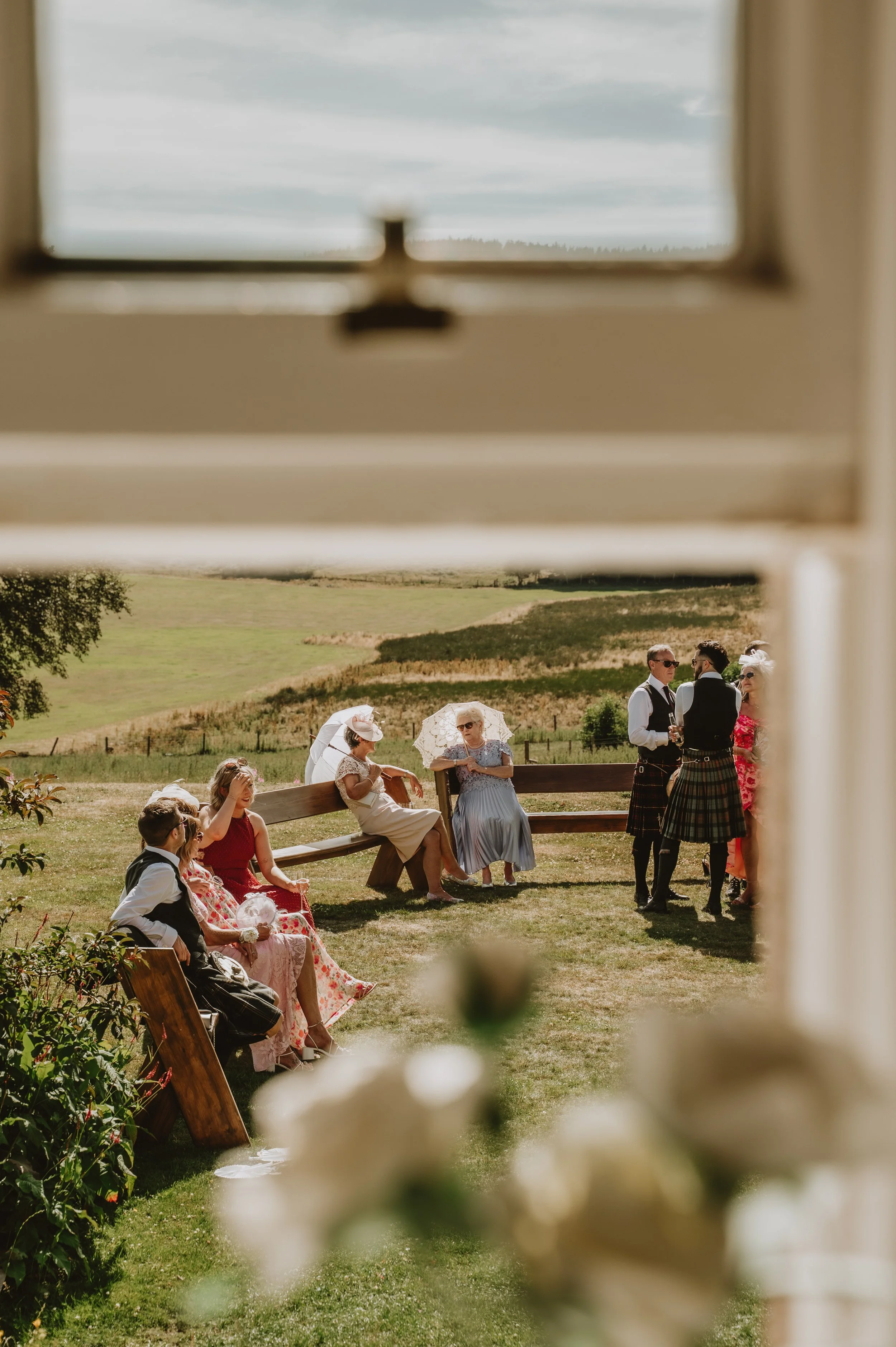 Wedding guests photographed through a window on a summer's day in Aberdeenshire, captured by Jules Williams Photography