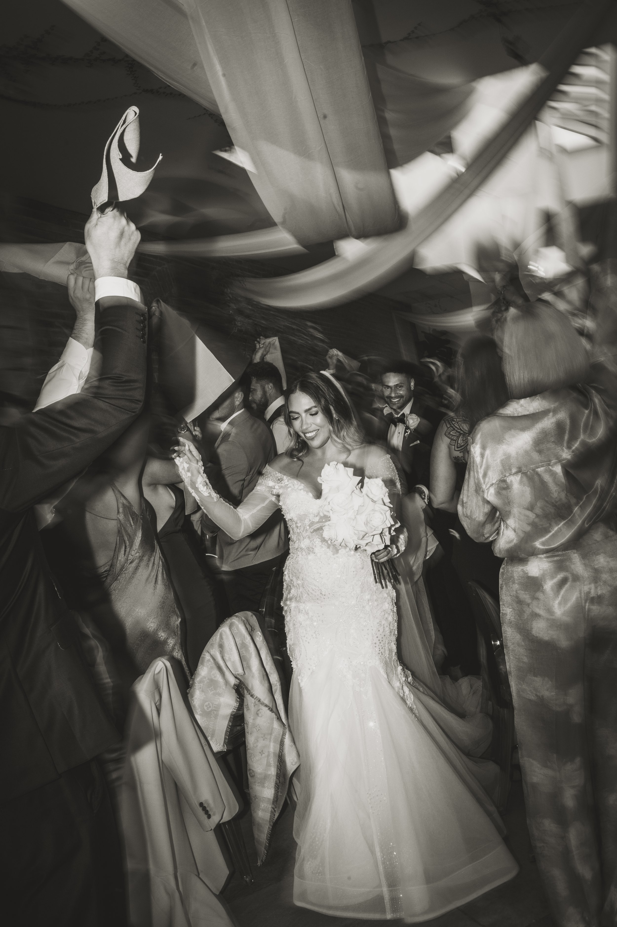 Bride dancing at a wedding reception with guests waving napkins.