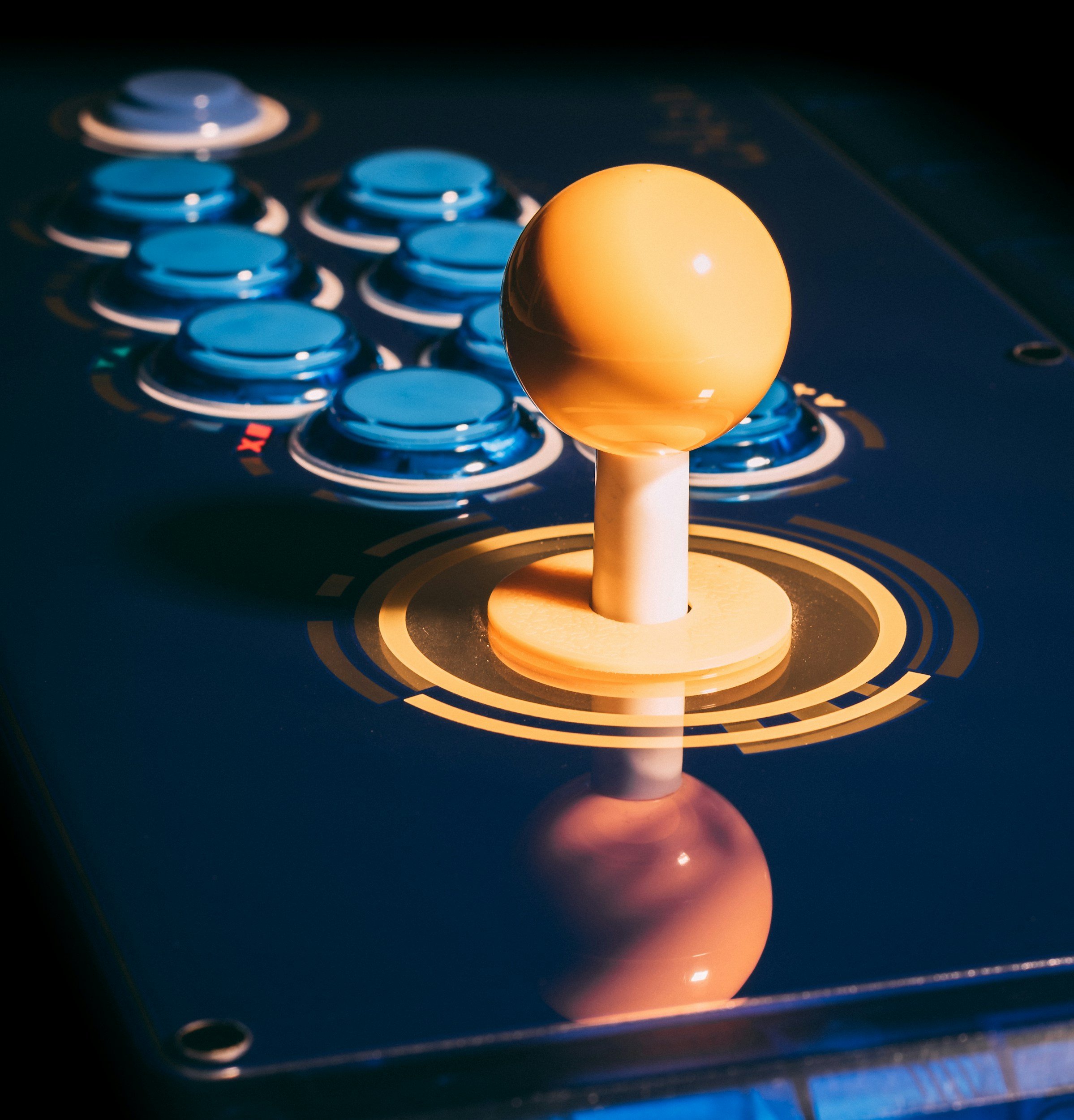 A futuristic arcade-style joystick with a yellow spherical handle and blue buttons on a dark surface.