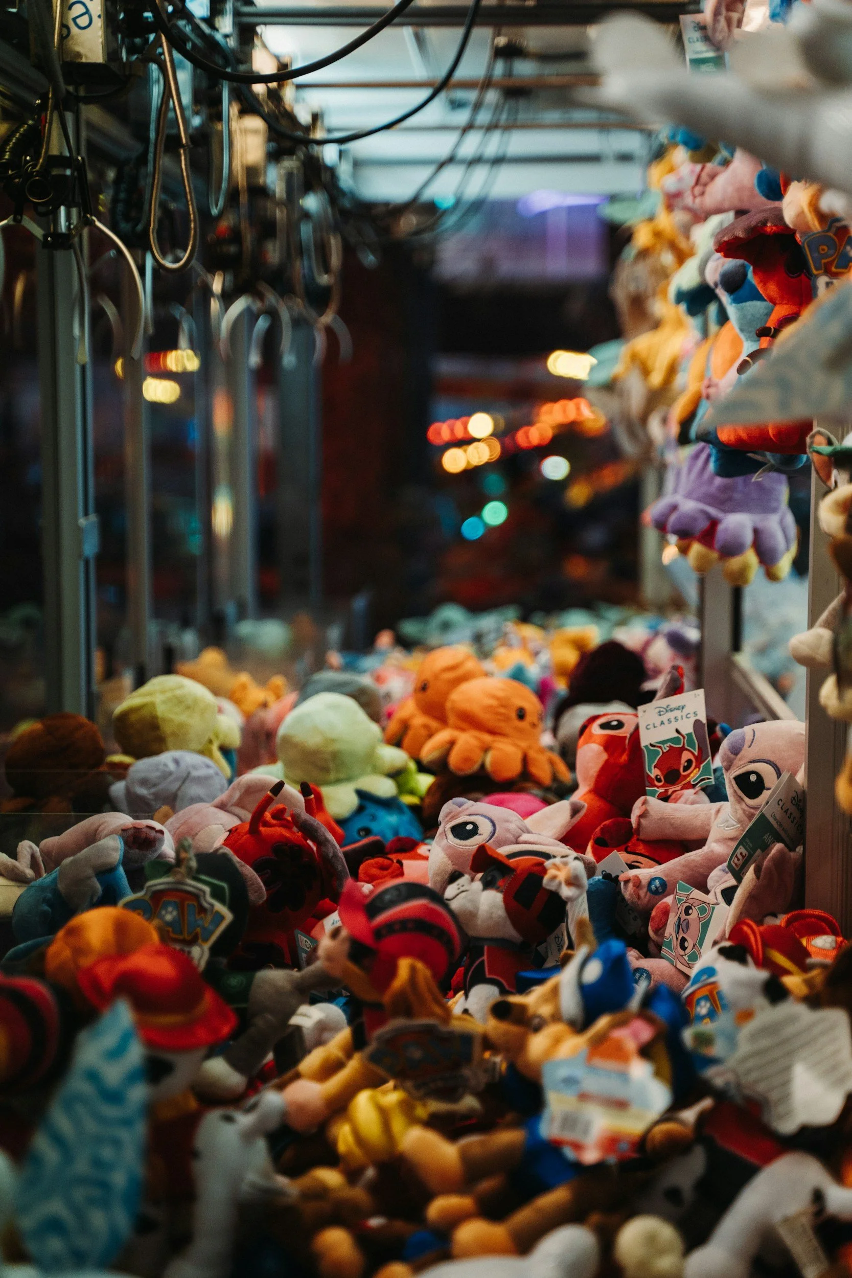 A display of colorful stuffed toys and plush dolls on a marketplace stall at night, with blurred city lights in the background.