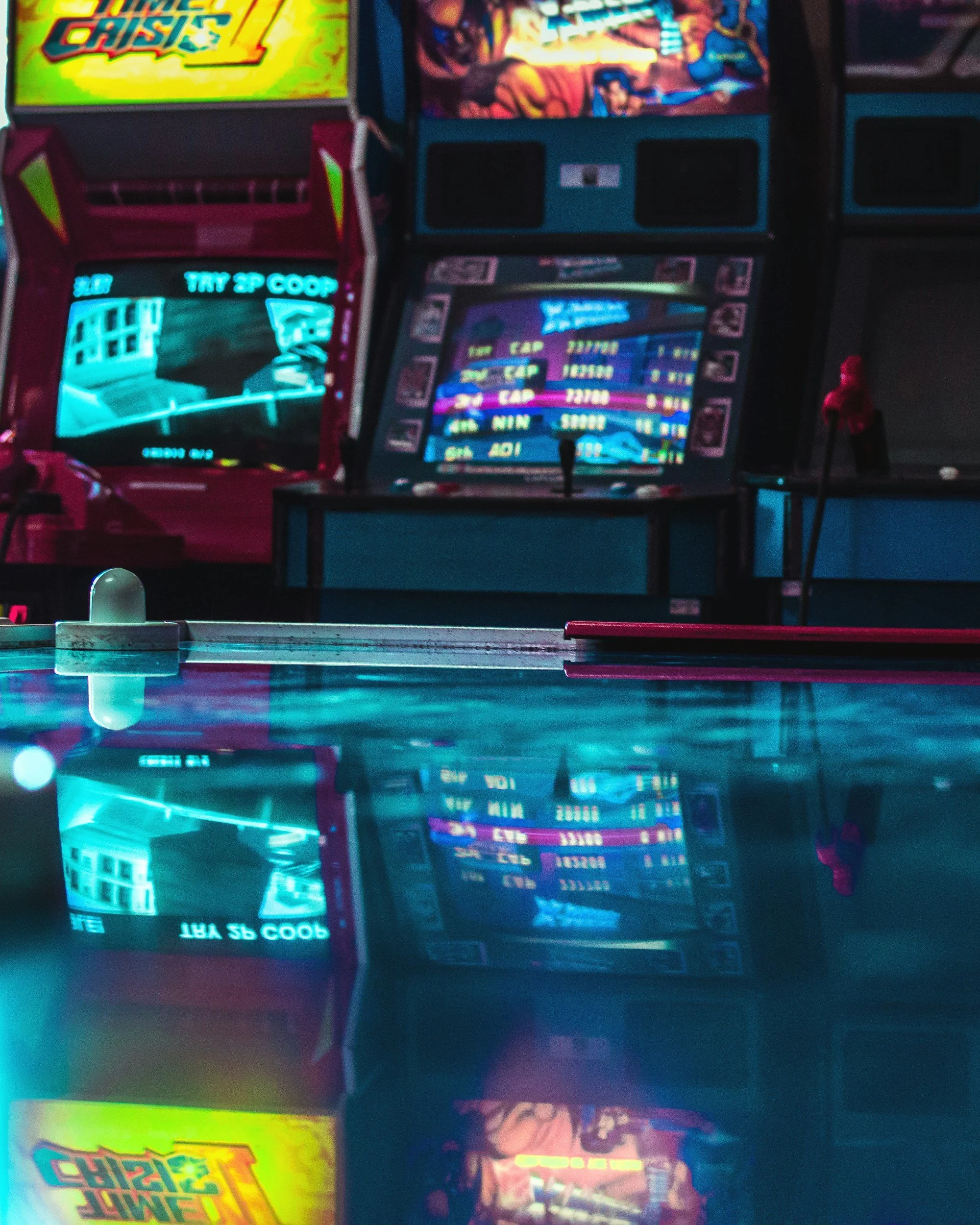 Record of the reflections of arcade game machines and a ping pong table with pink paddles in a dimly lit arcade.