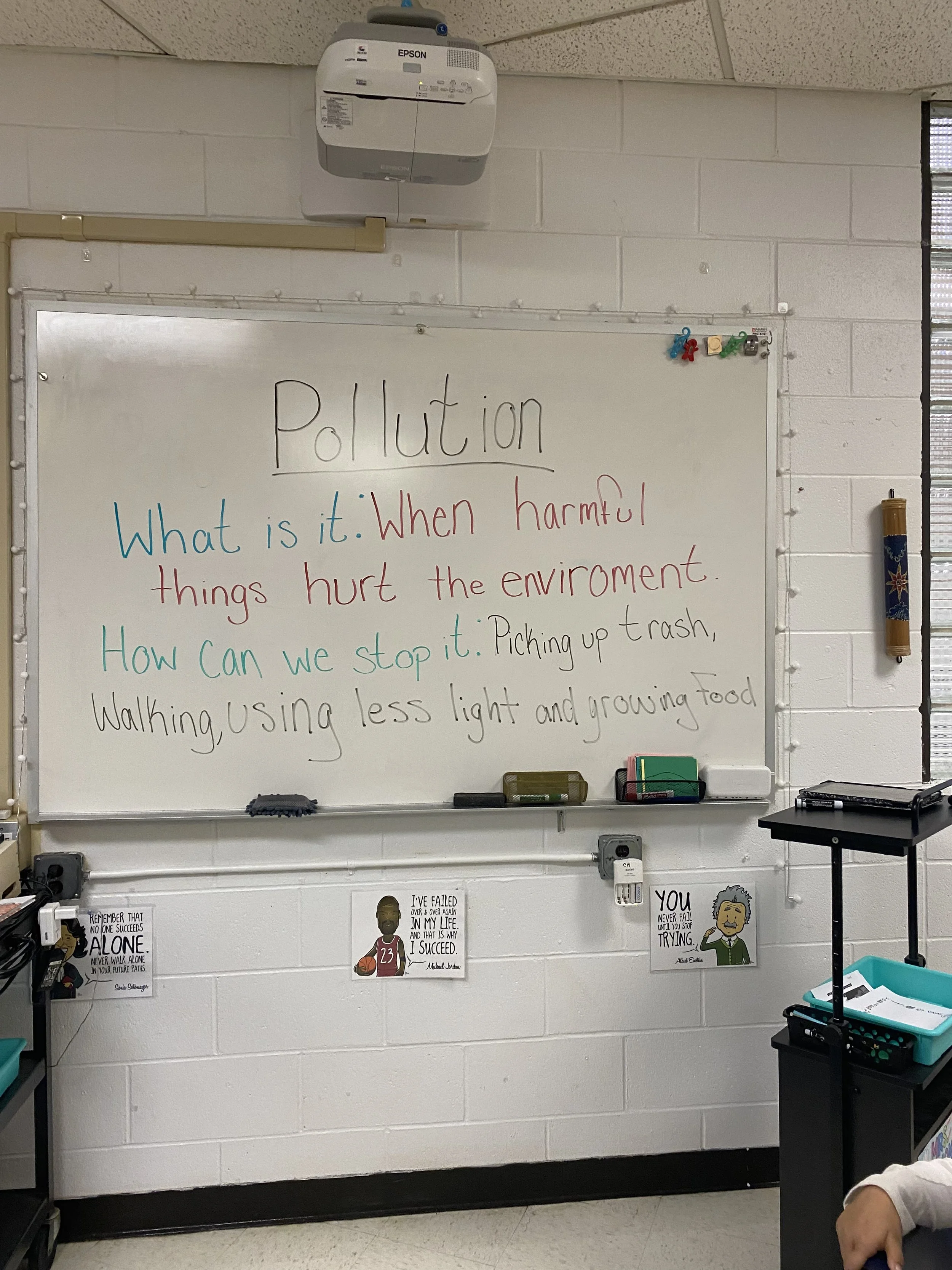 Whiteboard with a lesson about pollution, defining what it is and how to stop it, with motivational posters on the wall below.