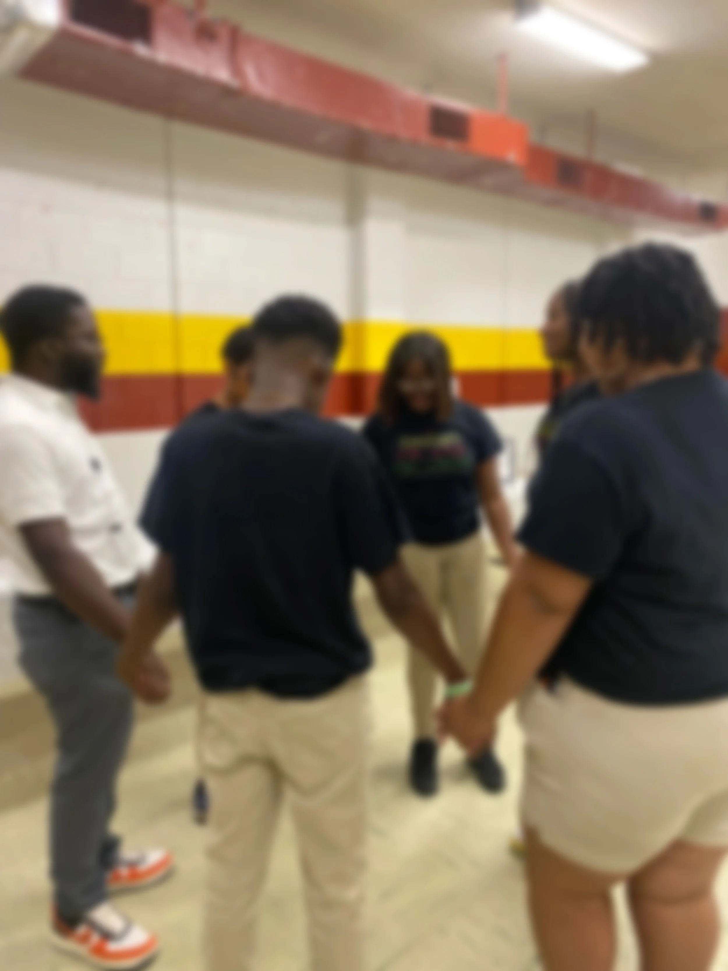 Blurry image of three people standing outdoors near a green, leafy background, viewed from behind.