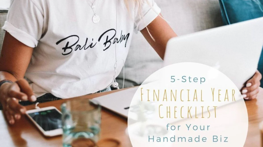 A woman wearing a white T-shirt with 'Bali Babe' printed on it, sitting at a table with a laptop, smartphone, glass of water, and a notebook, working on her business. Text overlay reads '5-Step Financial Year Checklist for Your Handmade Biz.'