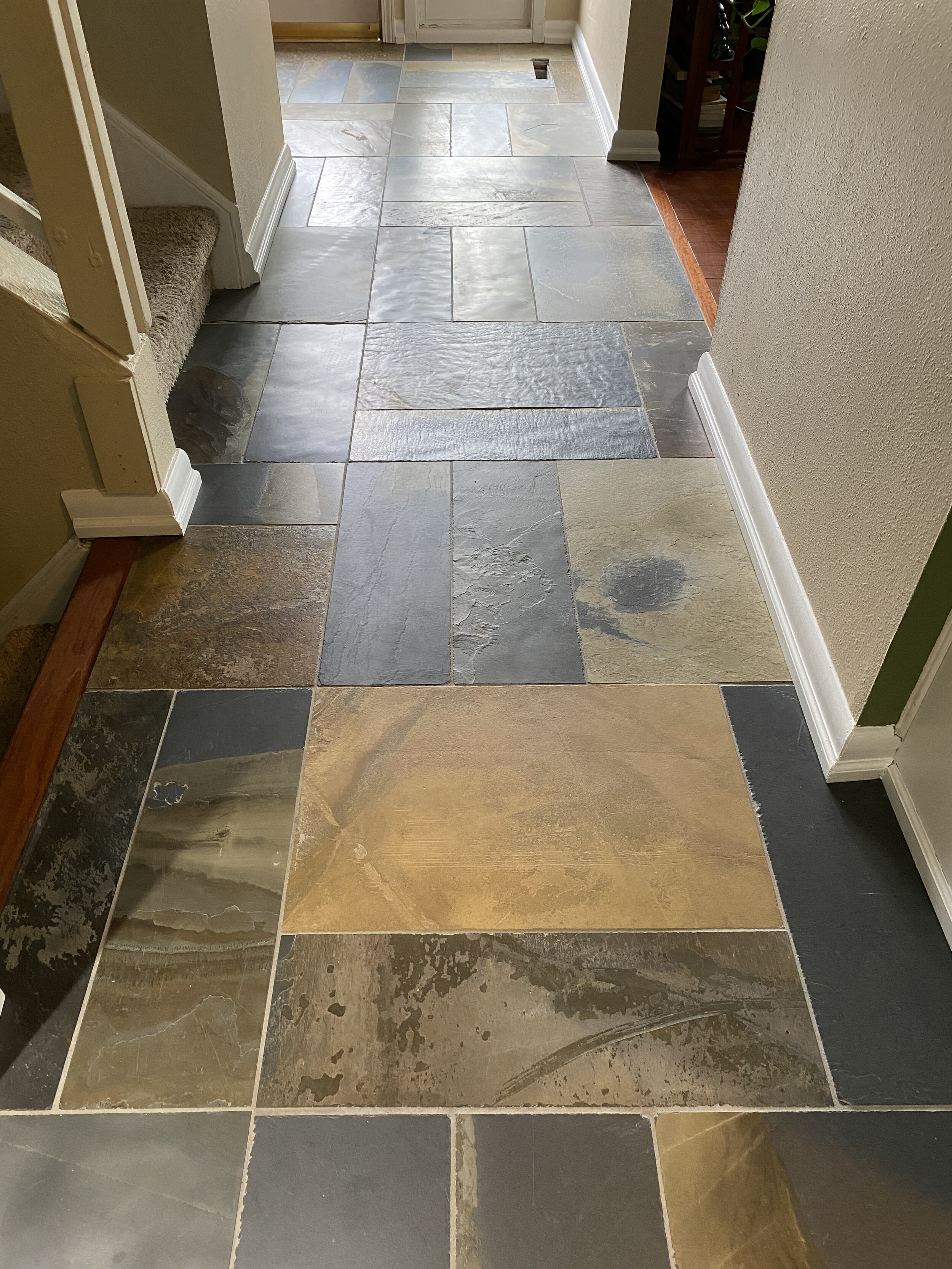 Interior view of a tiled entryway with multicolored slate tiles and white baseboards.