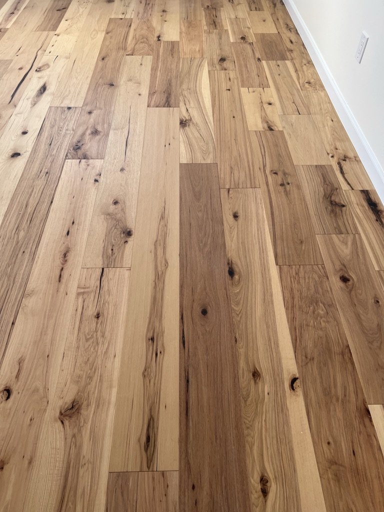 Wooden floor with natural-colored planks and visible knots, along with a white wall and baseboard.