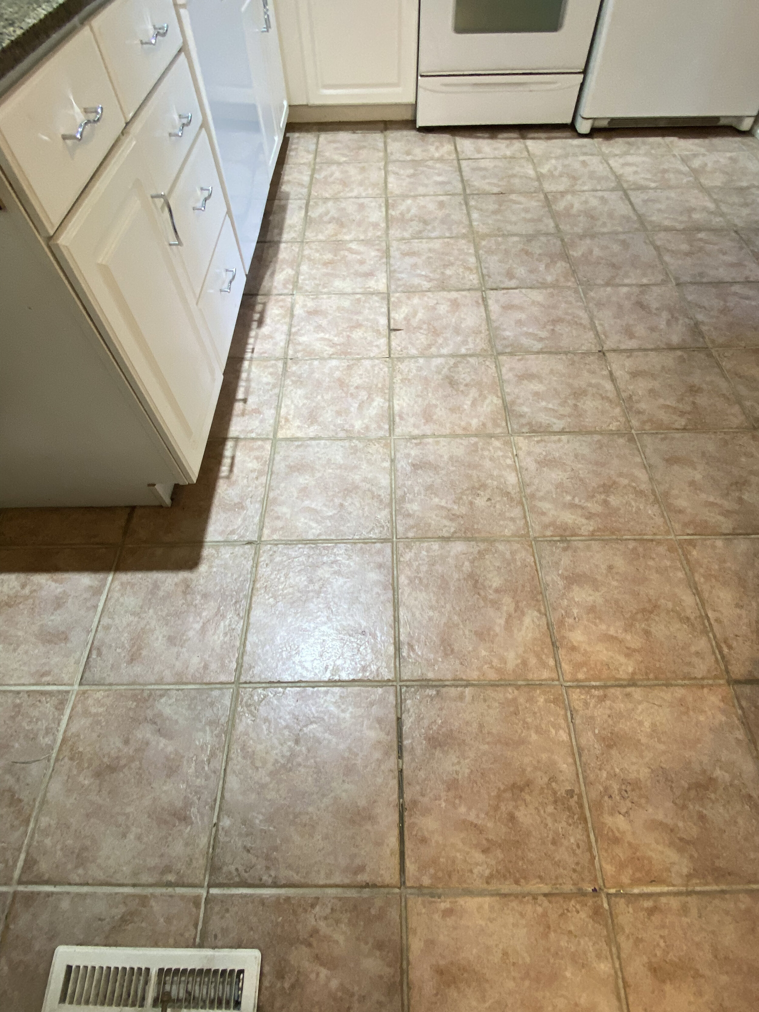 Kitchen floor with pinkish-brown ceramic tiles, white cabinets, oven, and refrigerator.