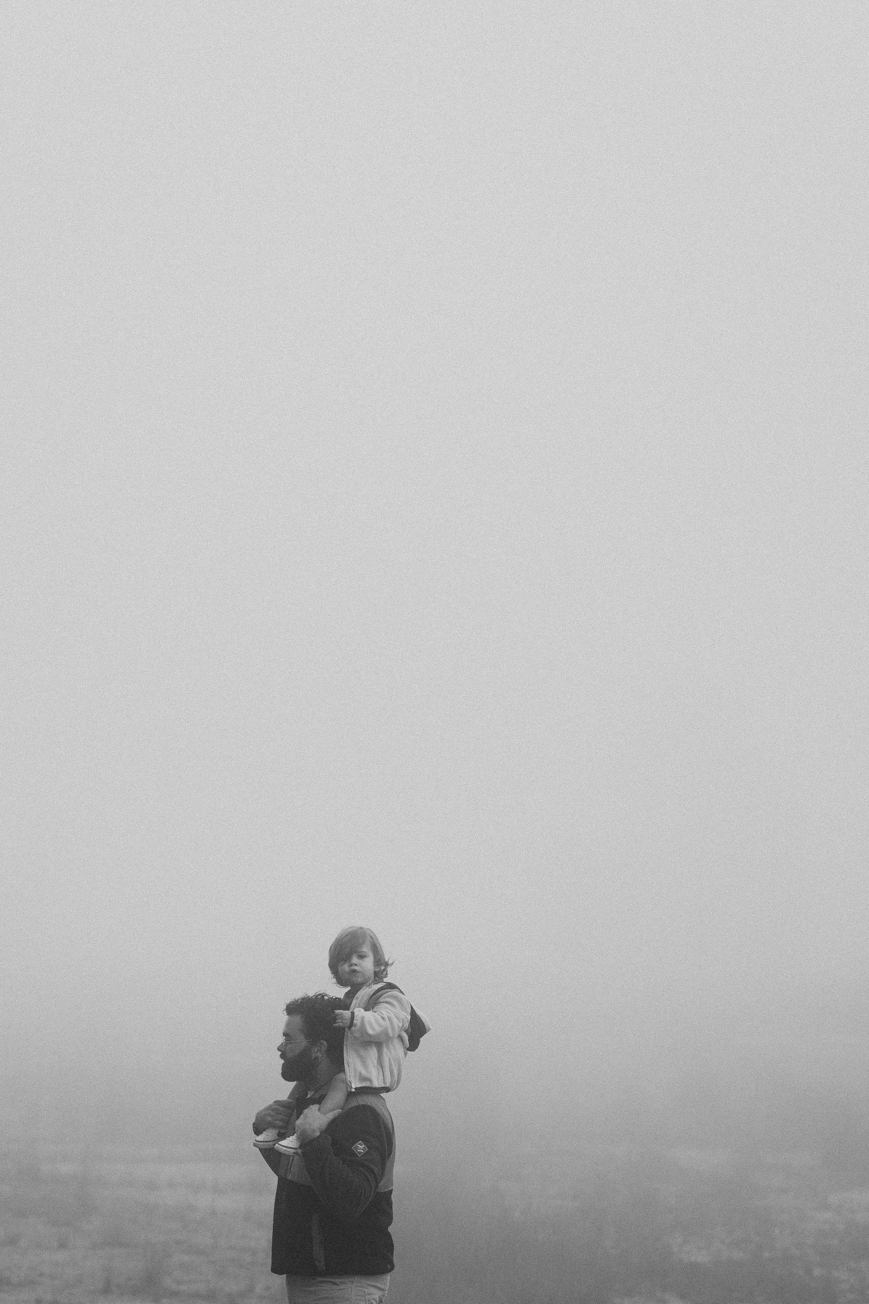 Een foto van een papa met zijn zoon op de schouders tijdens een mistige ochtend