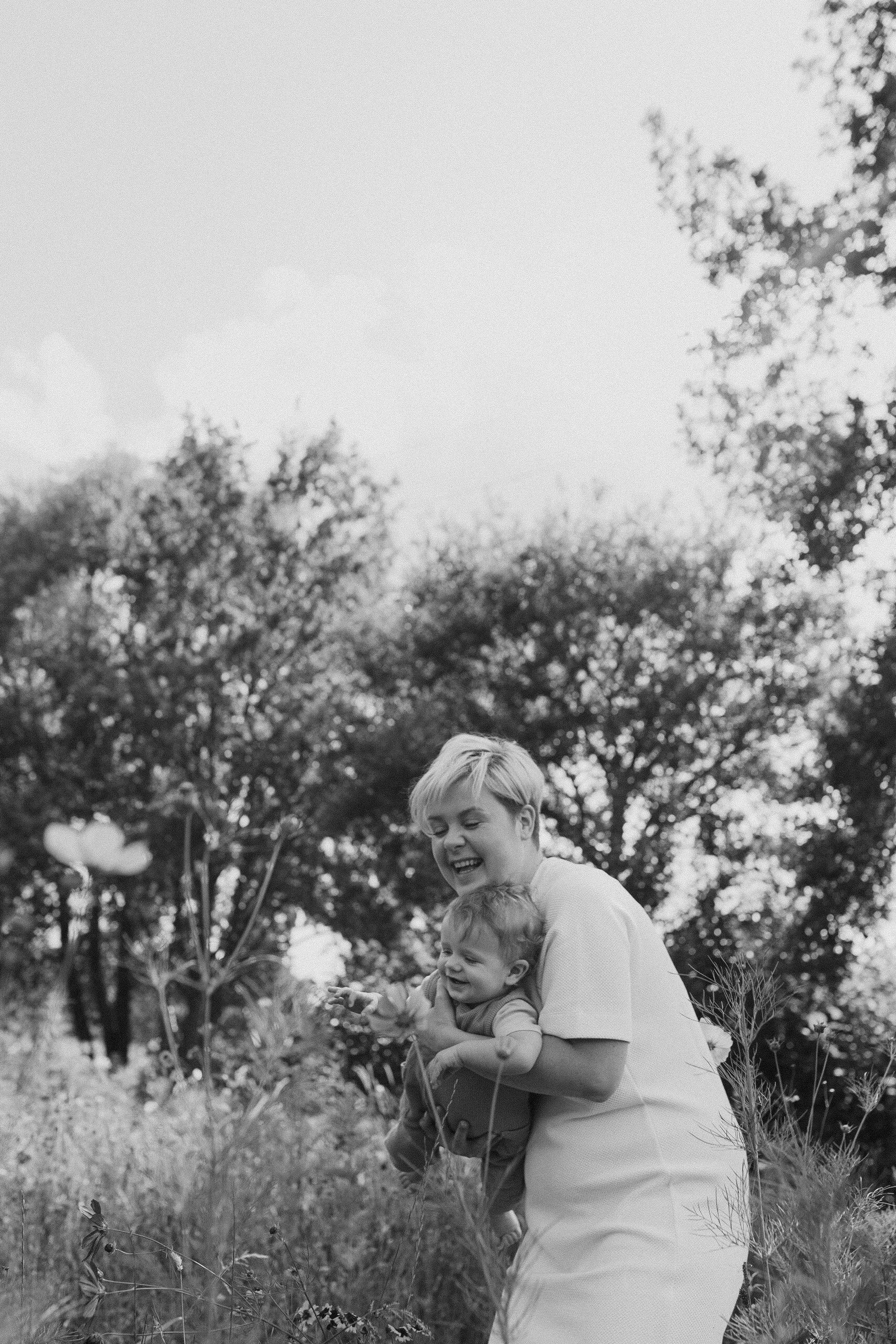Foto van een mama die met haar kind aan het spelen is tussen de bloemen in een weide in Balen