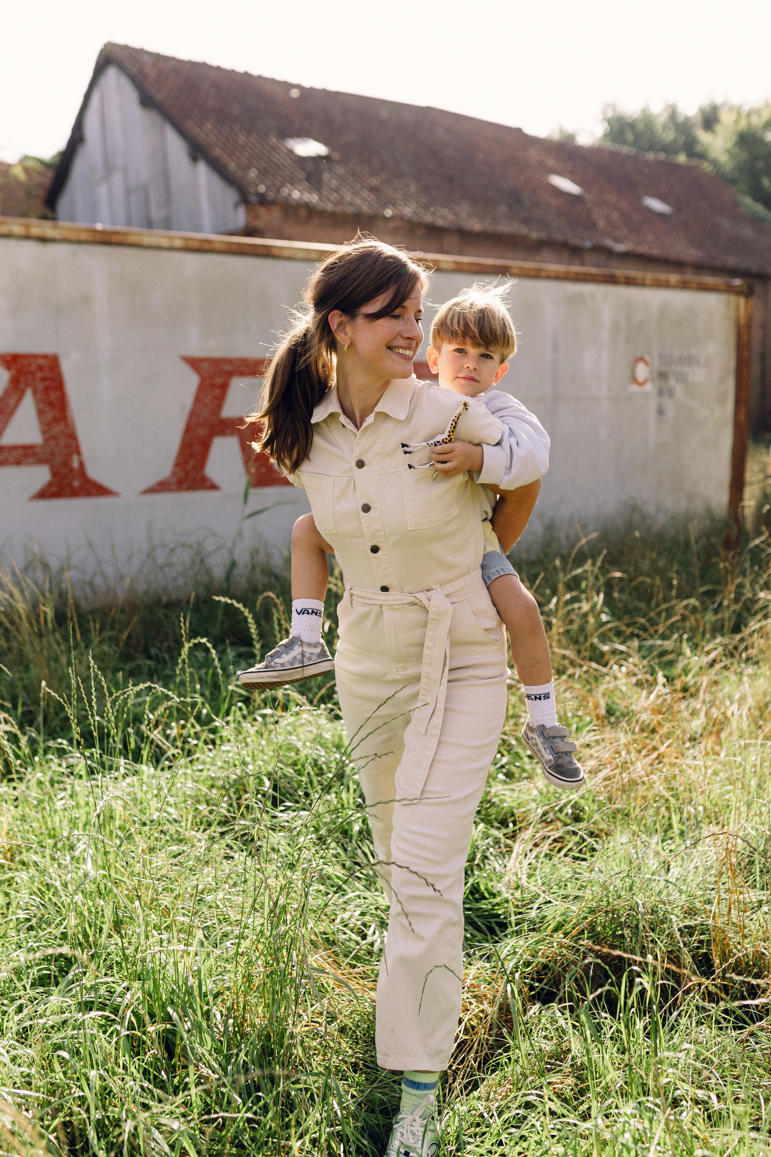 Portret van een mama met haar zoontje op de rug, wandelend door een weiland in Turnhout.