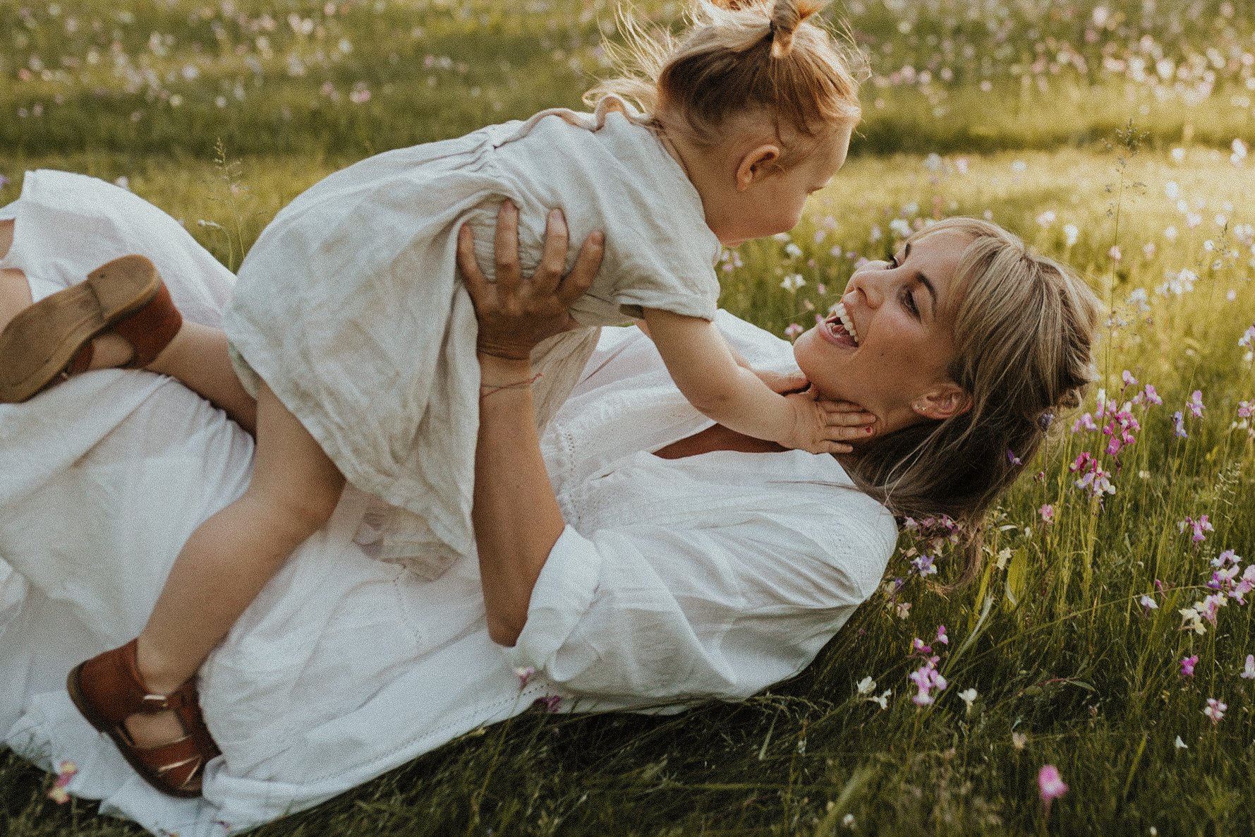 Een portret van een mama met haar dochtertje die samen spelen in een weide met bloemen