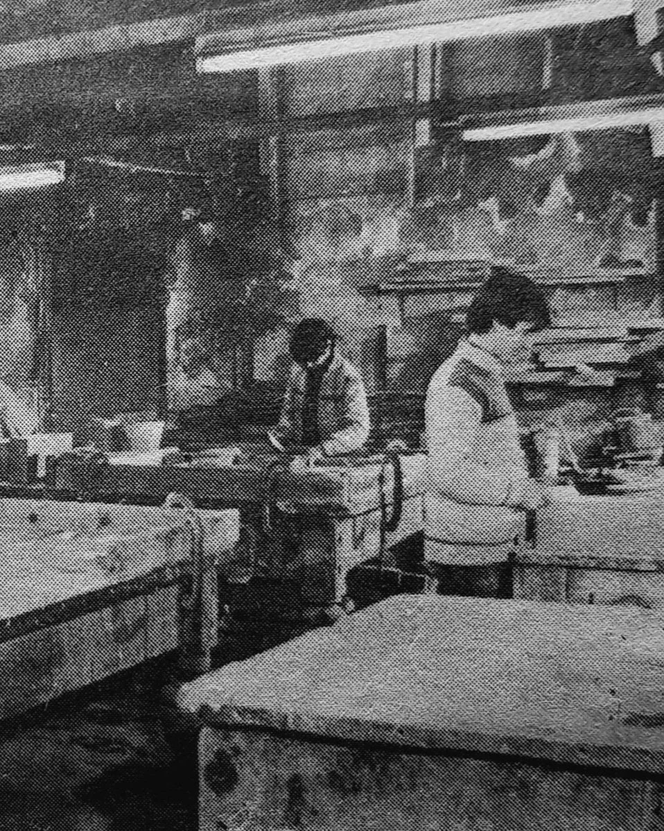 A photograph of an old work with two men working at the tables building fireplaces
