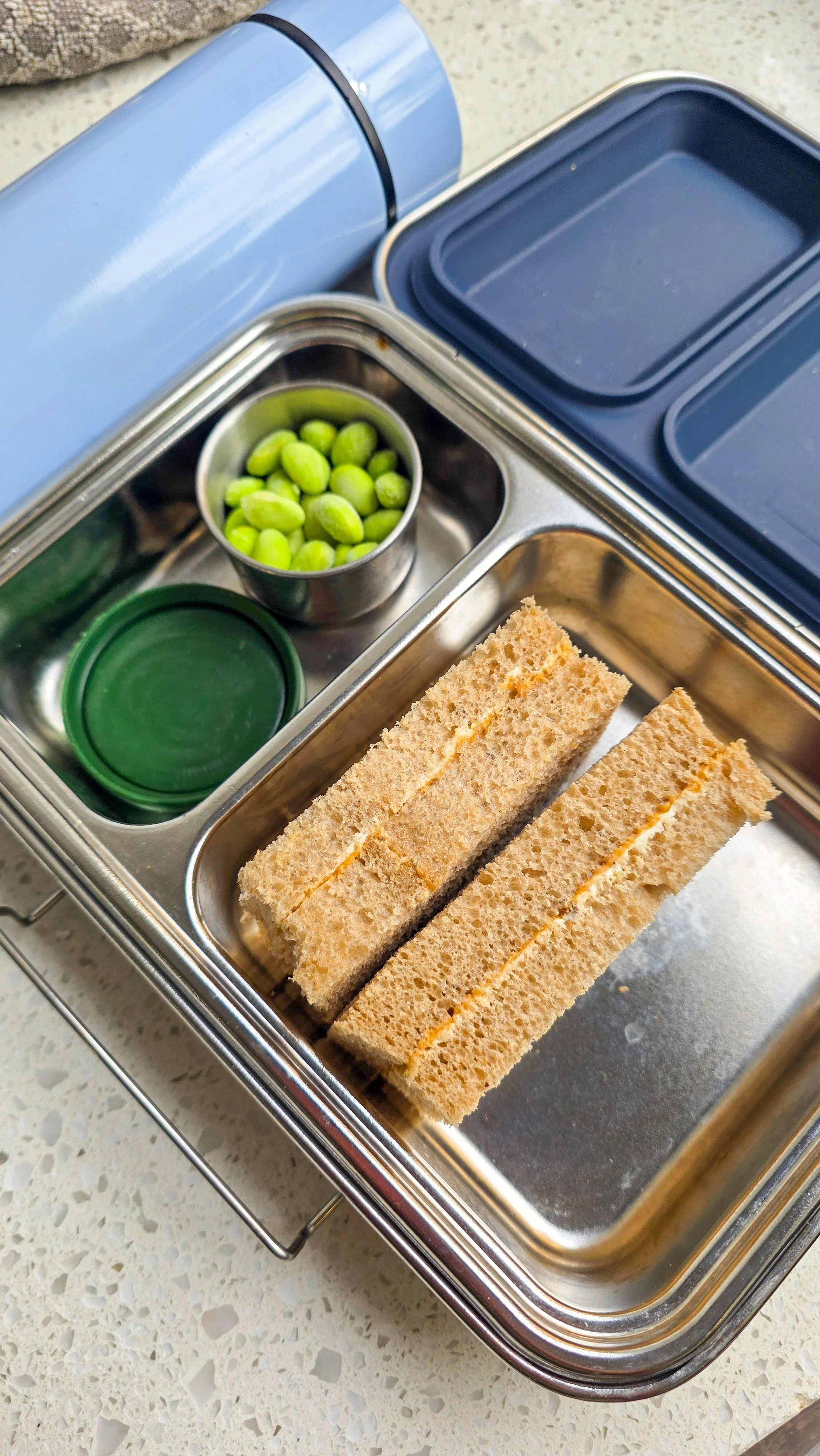 Kids lunchbox with peanut butter sandwich and edamame in a lunchbox