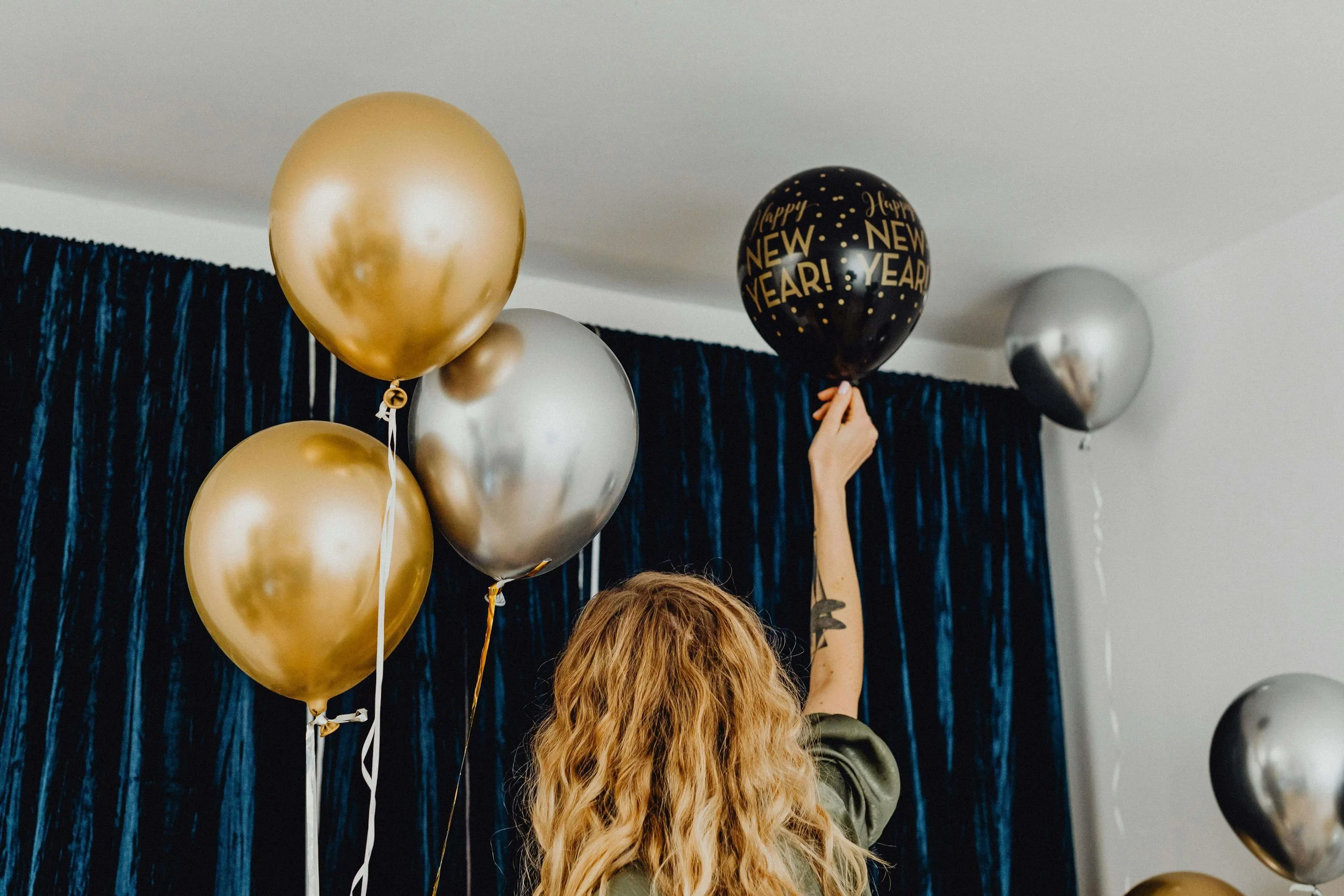 Person reaching up to hang New Year’s balloons, symbolizing pressure around resolutions, control, and anxiety therapy for restrictive eating in Erie, PA.