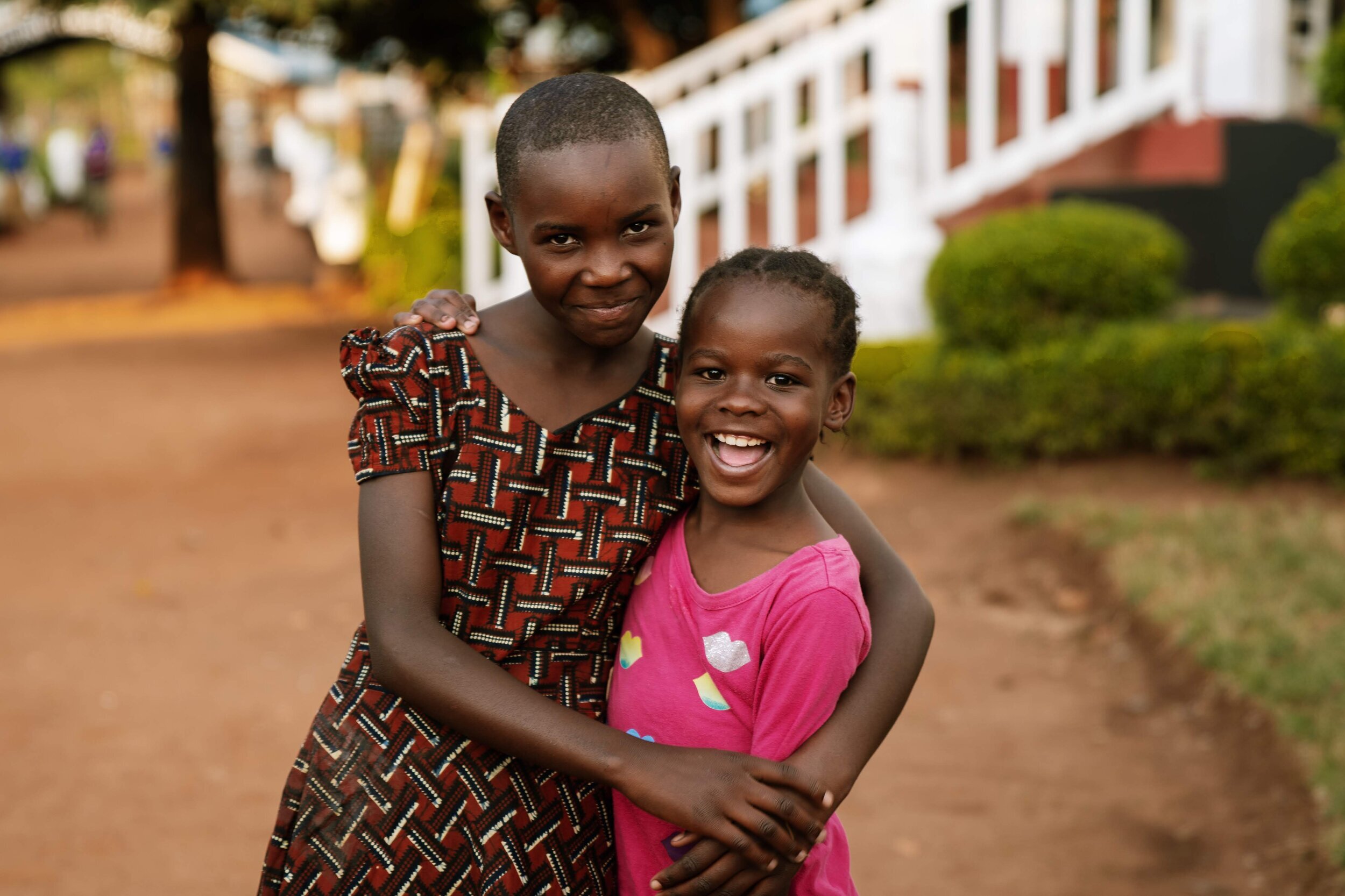 One young girl hugs another, both are grinning