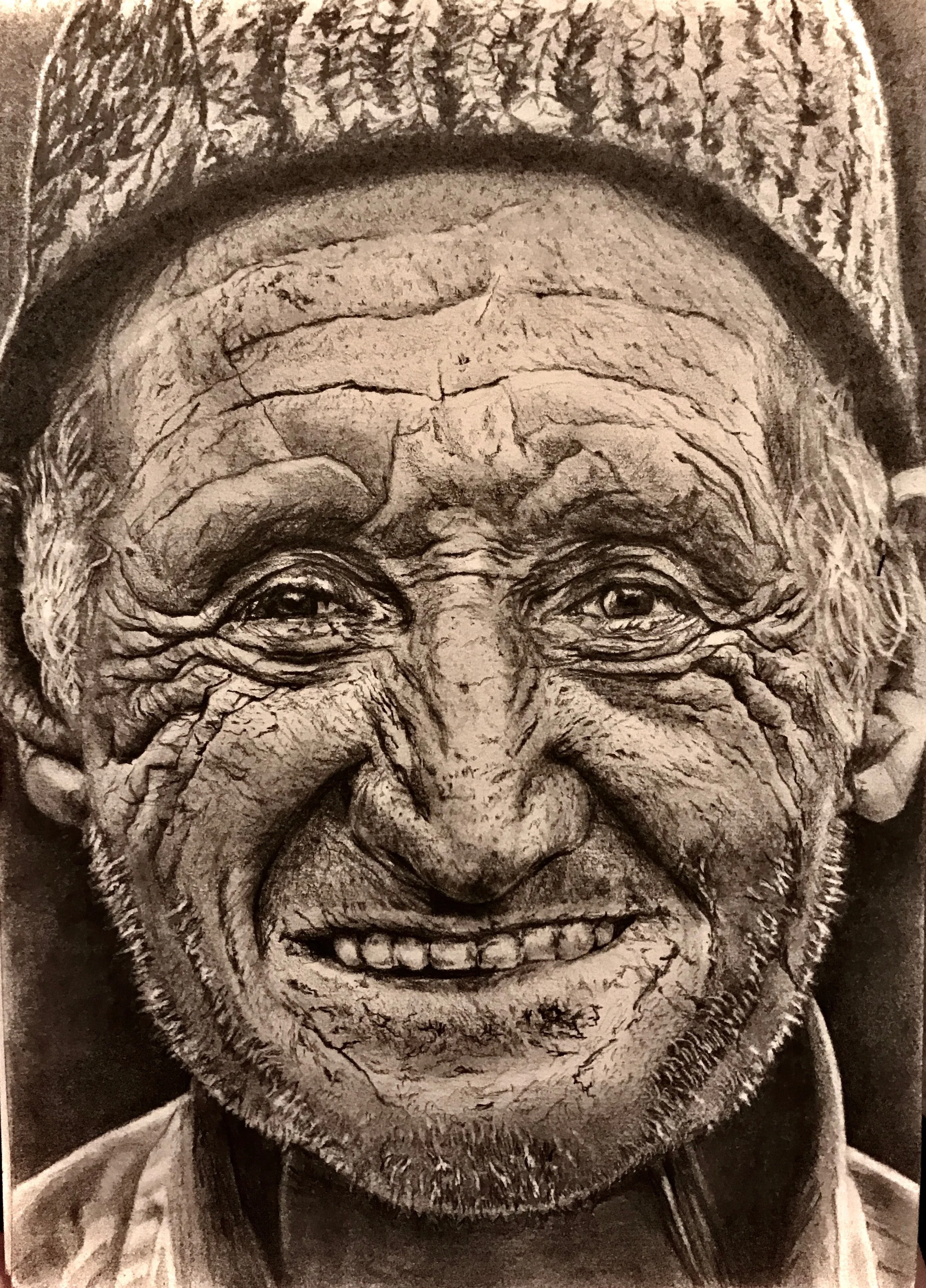 Black and white close-up photograph of an elderly man with a weathered face, smiling with eyes slightly squinted, wearing a patterned cap and a jacket.