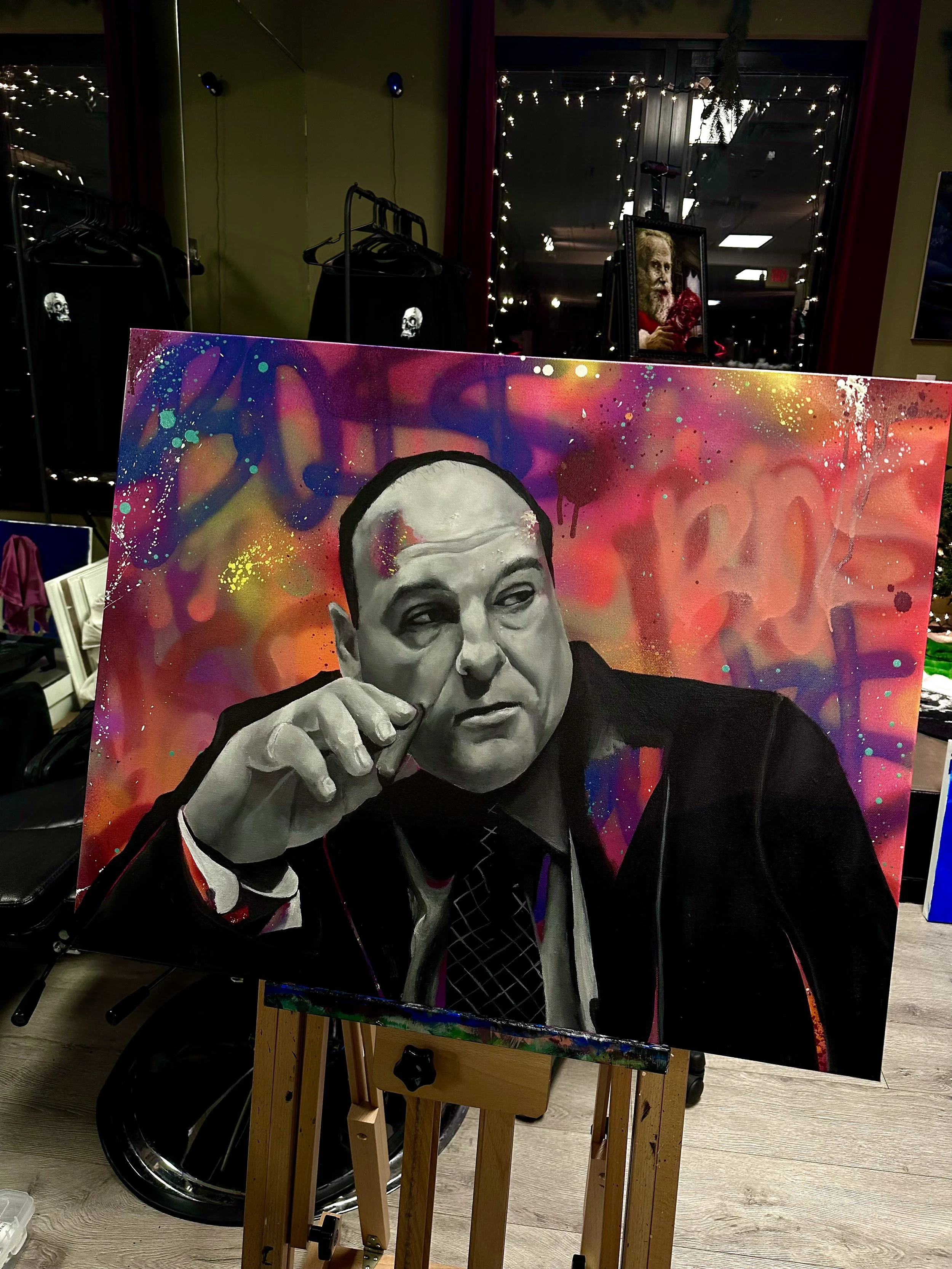 Black and white portrait of a man with slicked-back hair, sitting with his hand near his face, against a colorful abstract background with splashes of pink, orange, purple, and yellow