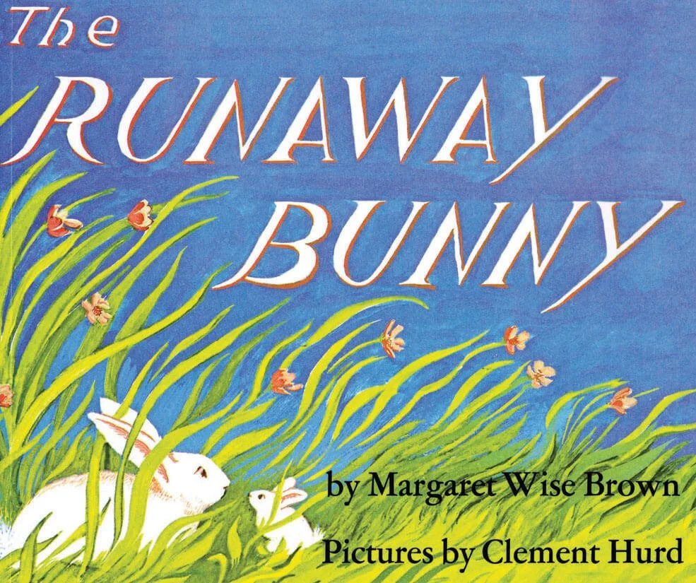 A mother and child rabbit sit in a field of tall grass with flowers against a blue sky