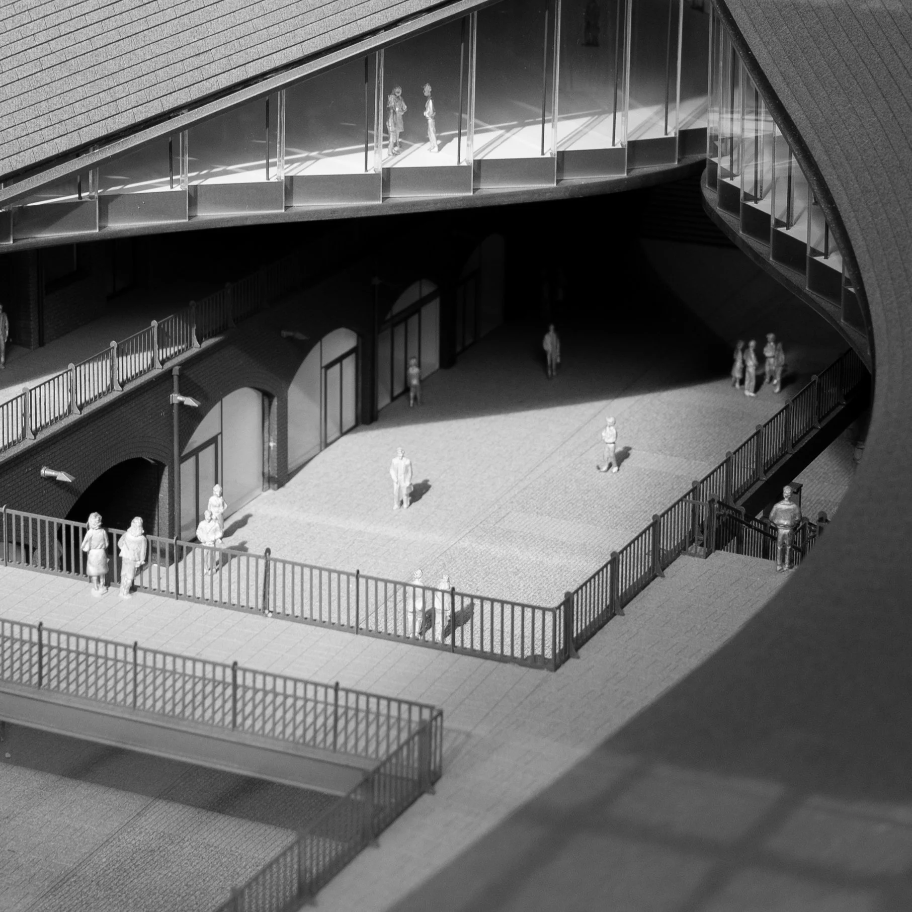Black and white architectural model of a multi-level building with balconies, walkways, and small figurines representing people on the different levels.