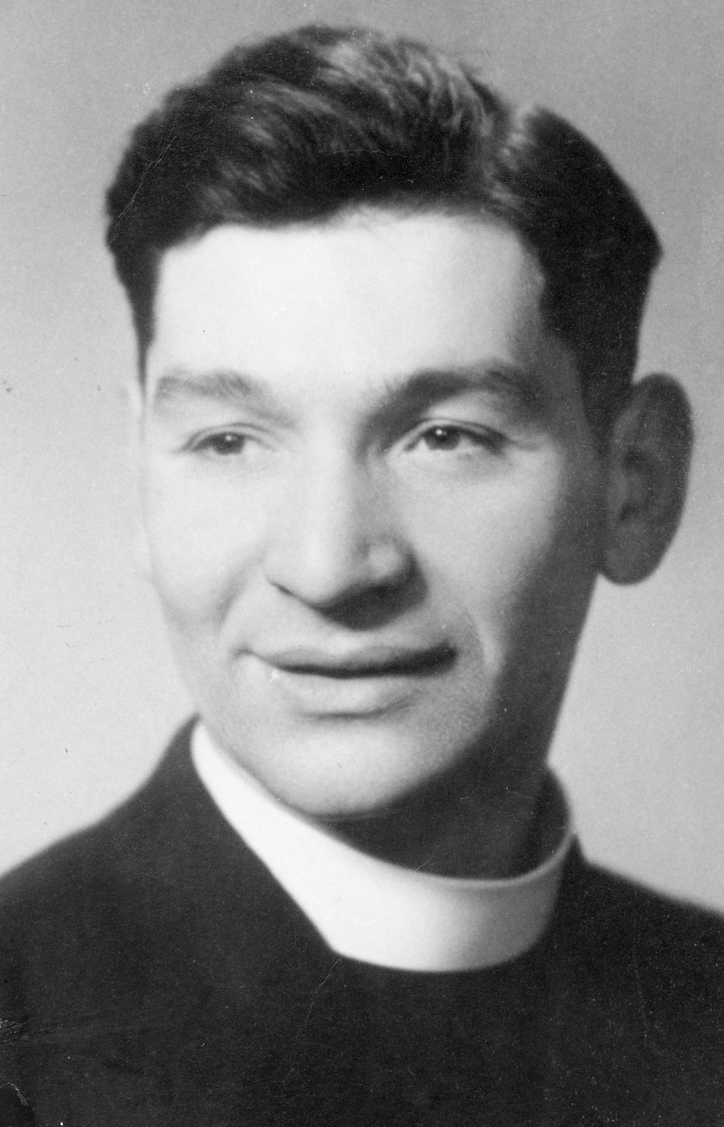 Black and white photo of a young man with dark, neatly styled hair, wearing a dark suit and white shirt, with a slight smile.