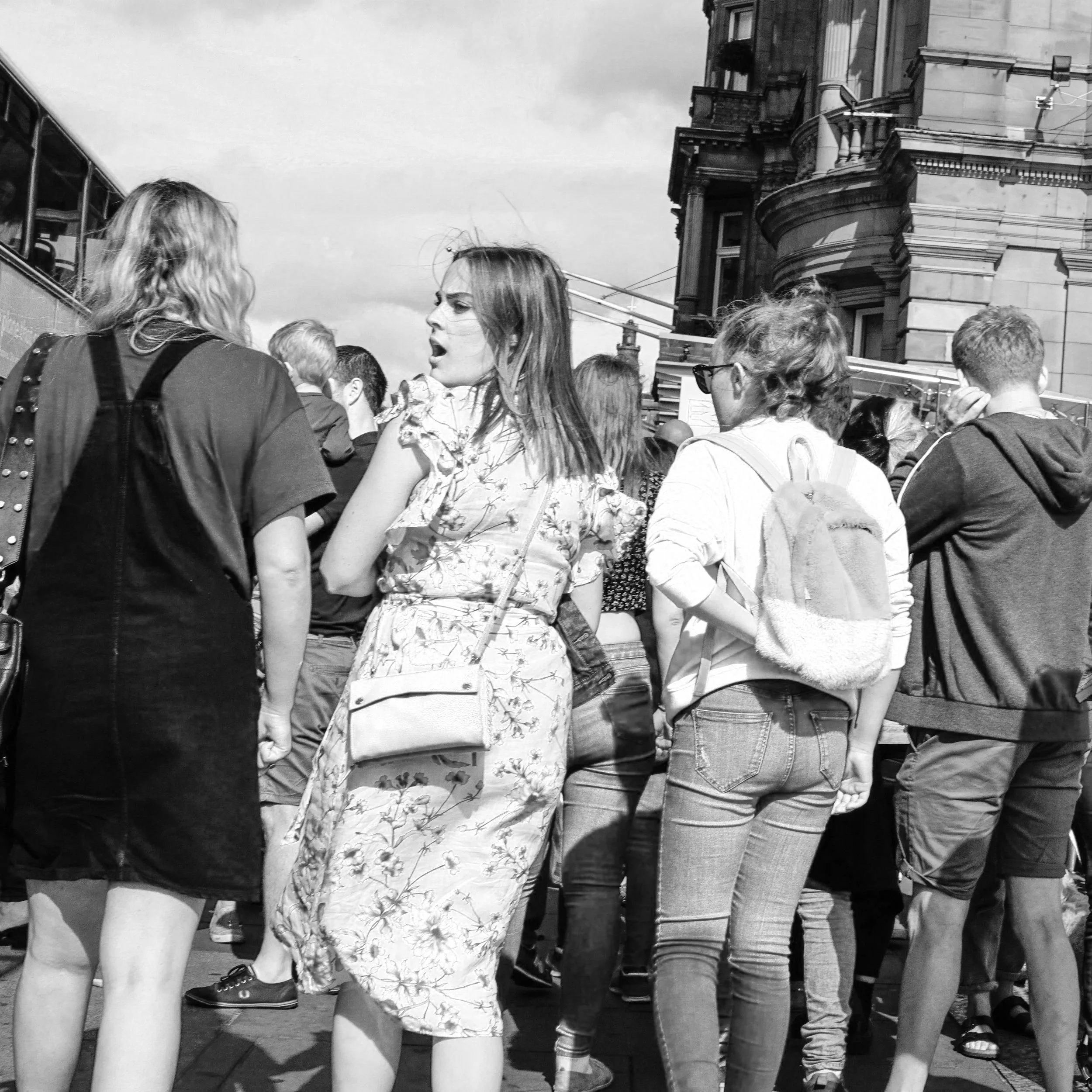 People standing in a line outdoors near historical buildings, viewed from behind; black and white photo.