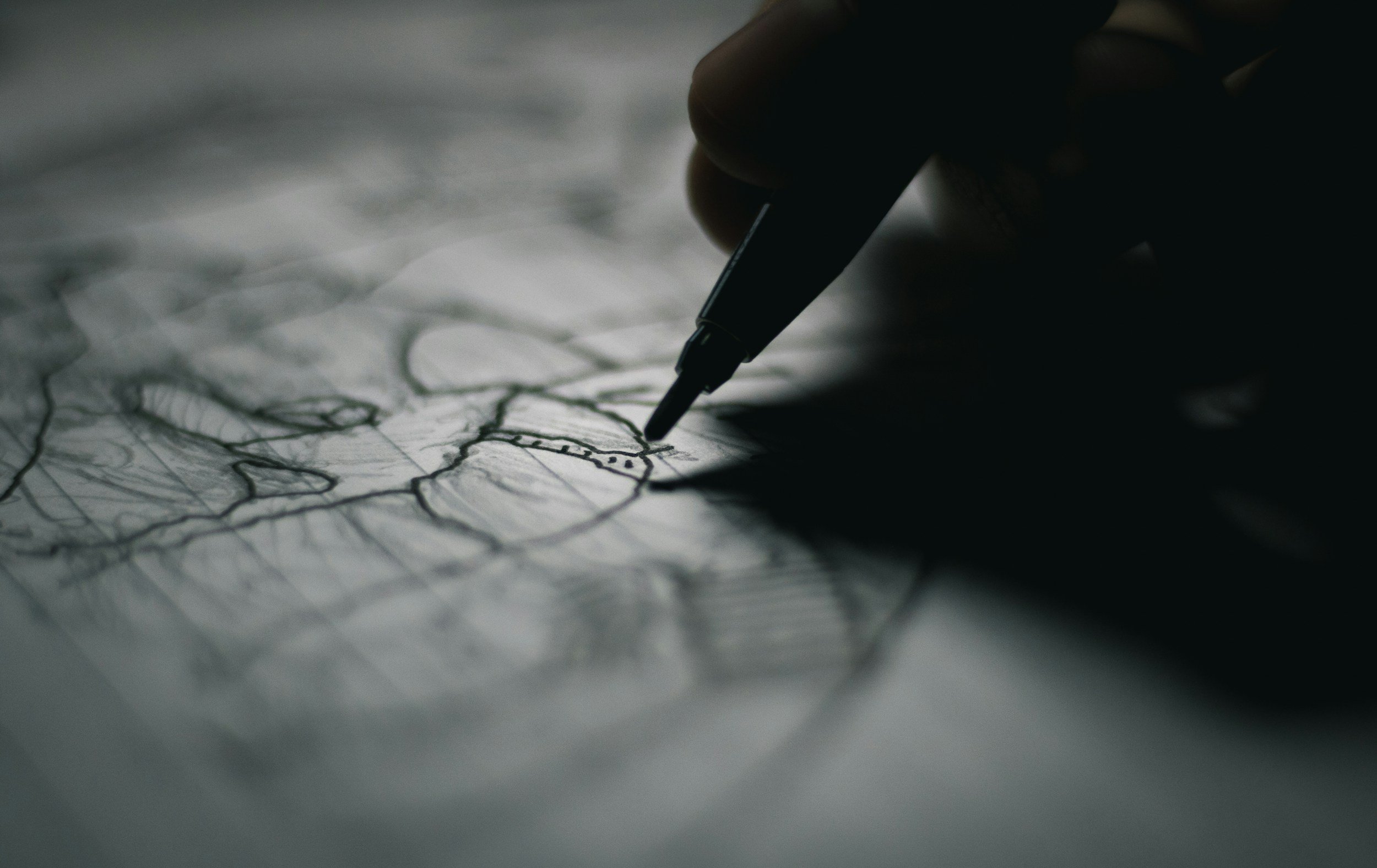 A hand holding a black pen drawing sketches on a sheet of paper in a dark setting.