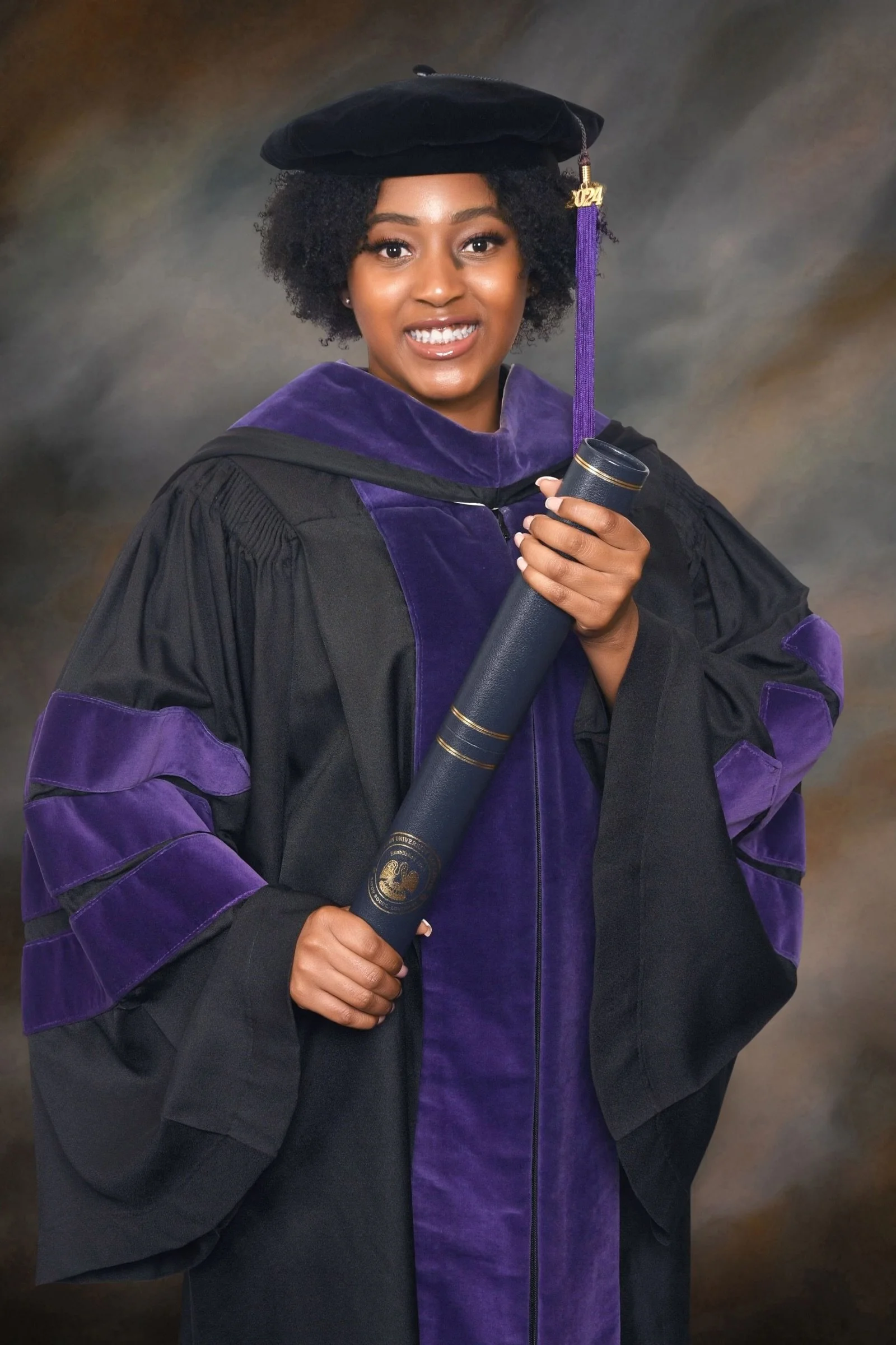 A woman in a graduation gown and cap holding a diploma, smiling at the camera.