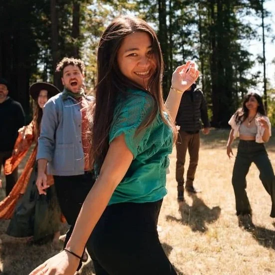 Group of people dancing and socializing in a warmly lit wooden room with plants and nature-inspired décor.