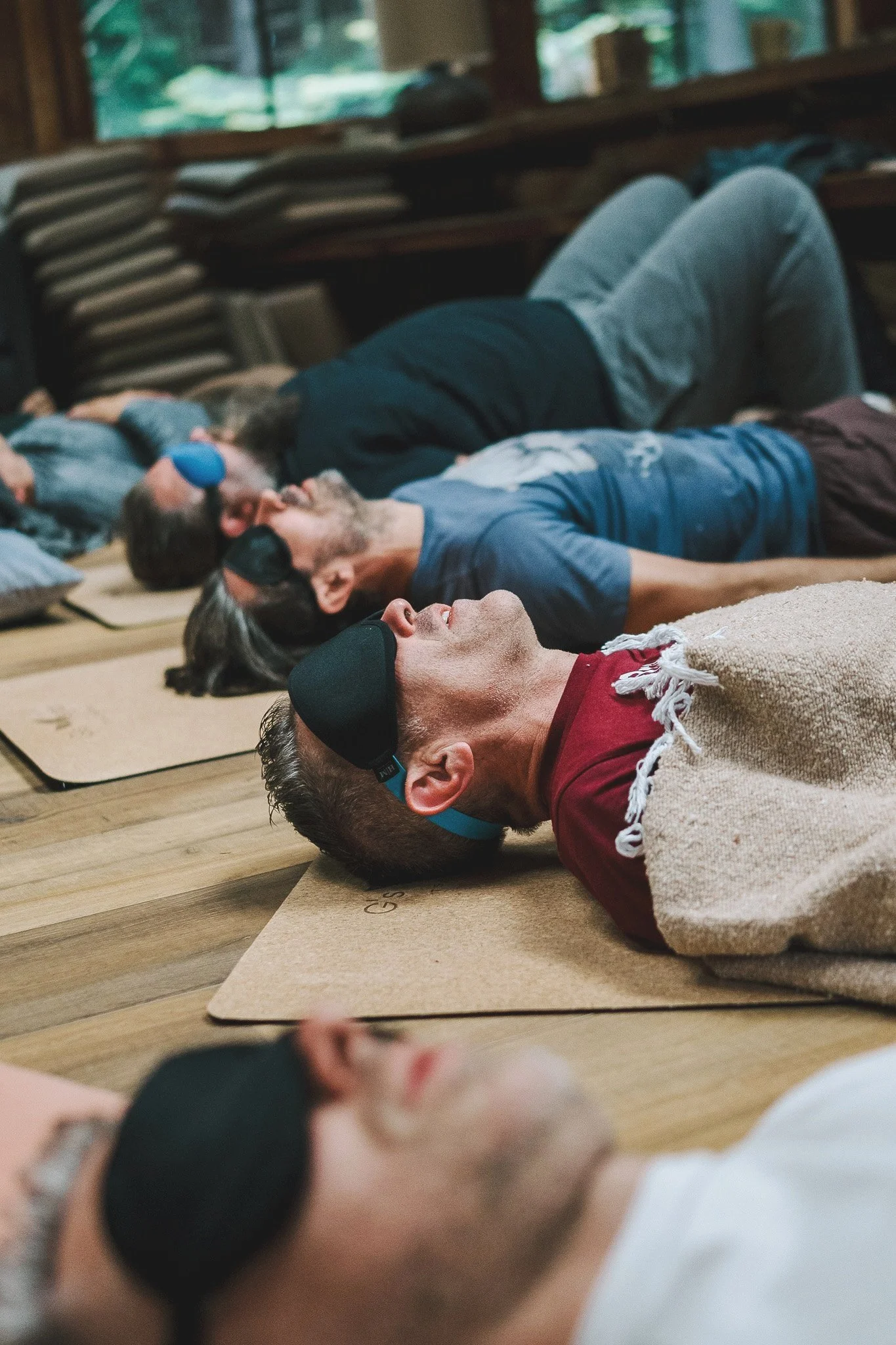 People practicing relaxation or meditation lying on mats with eyes covered in a rustic indoor space.