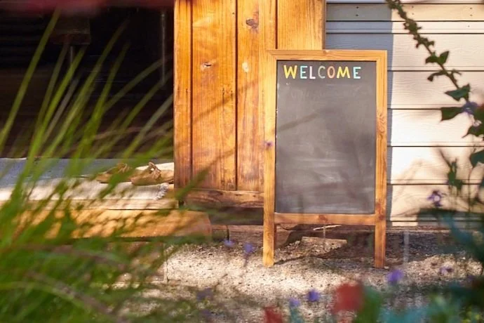 Wooden welcome signboard outside a building with a blackboard for writing.