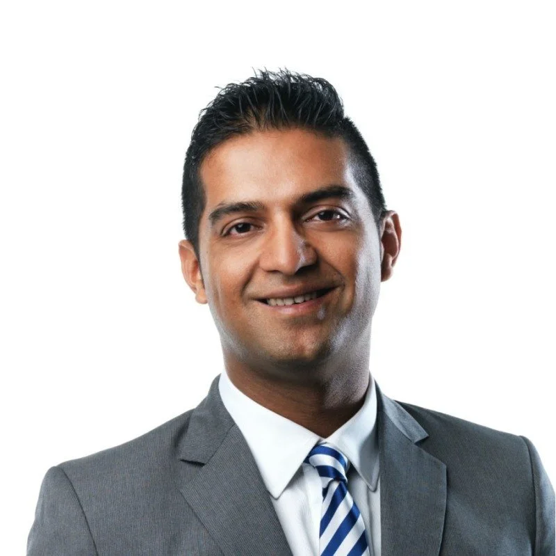 Professional portrait of a man in a gray suit with a striped tie, smiling against a plain white background.