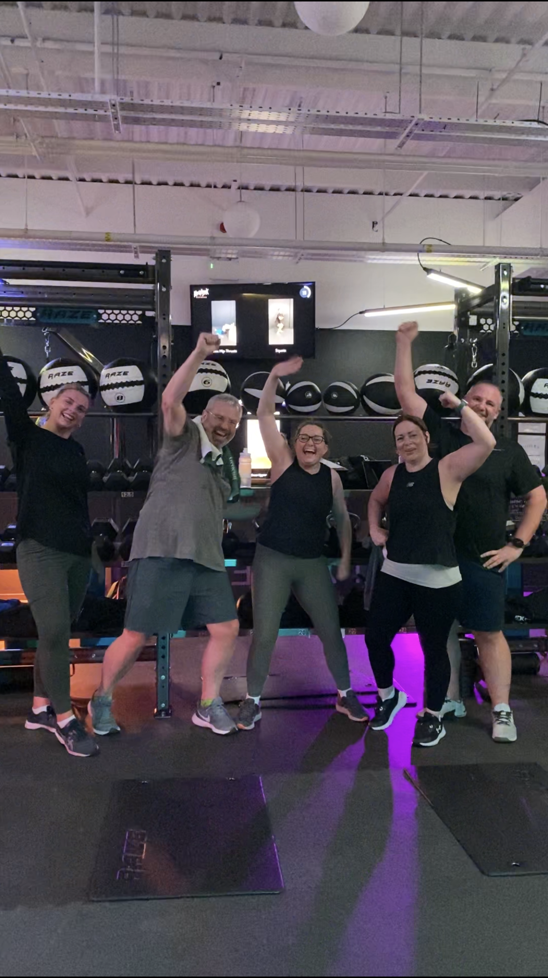 Group of 5 gym members smiling and cheering to the camera.