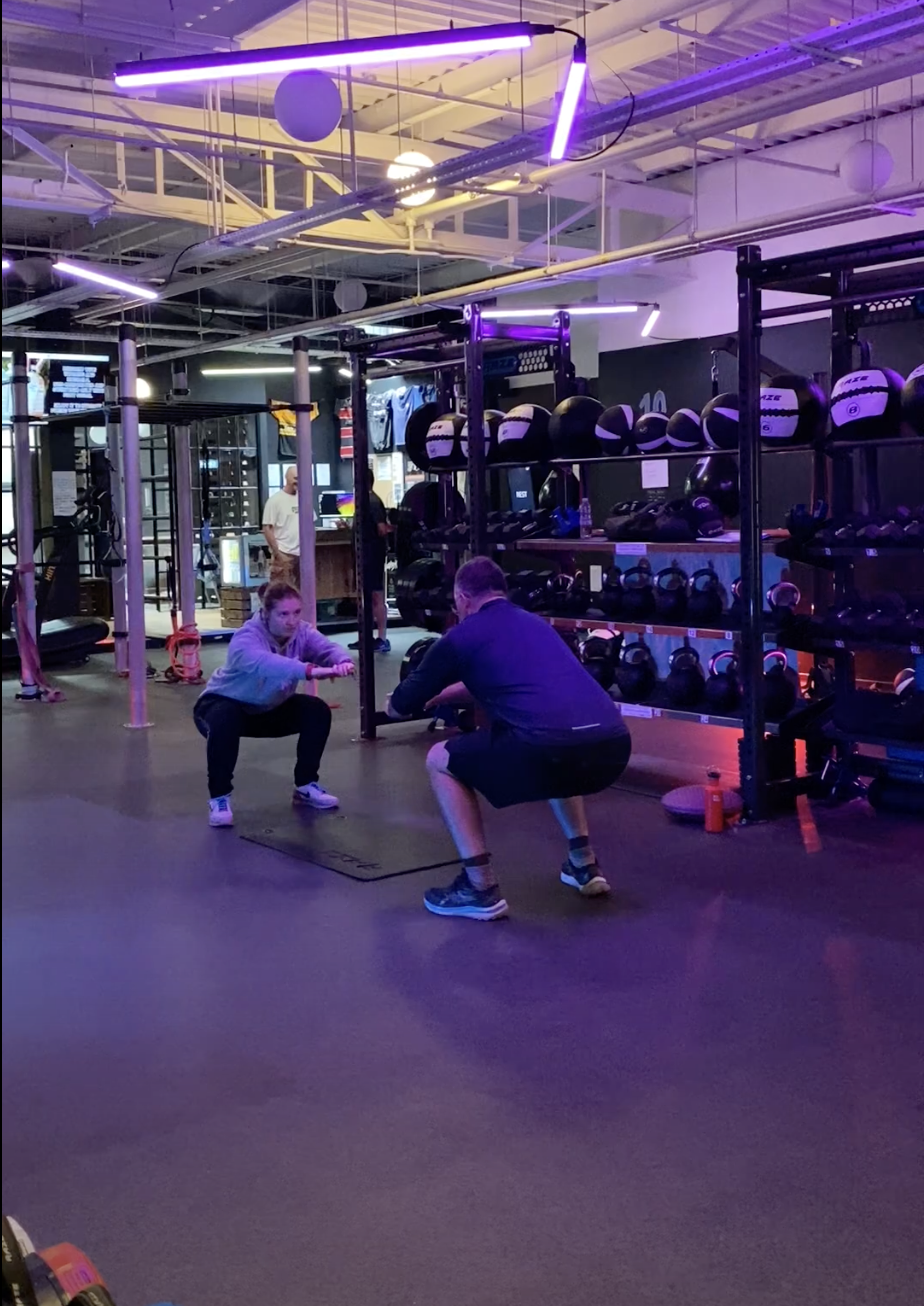 Coach demonstrating correct squat position to gym member.