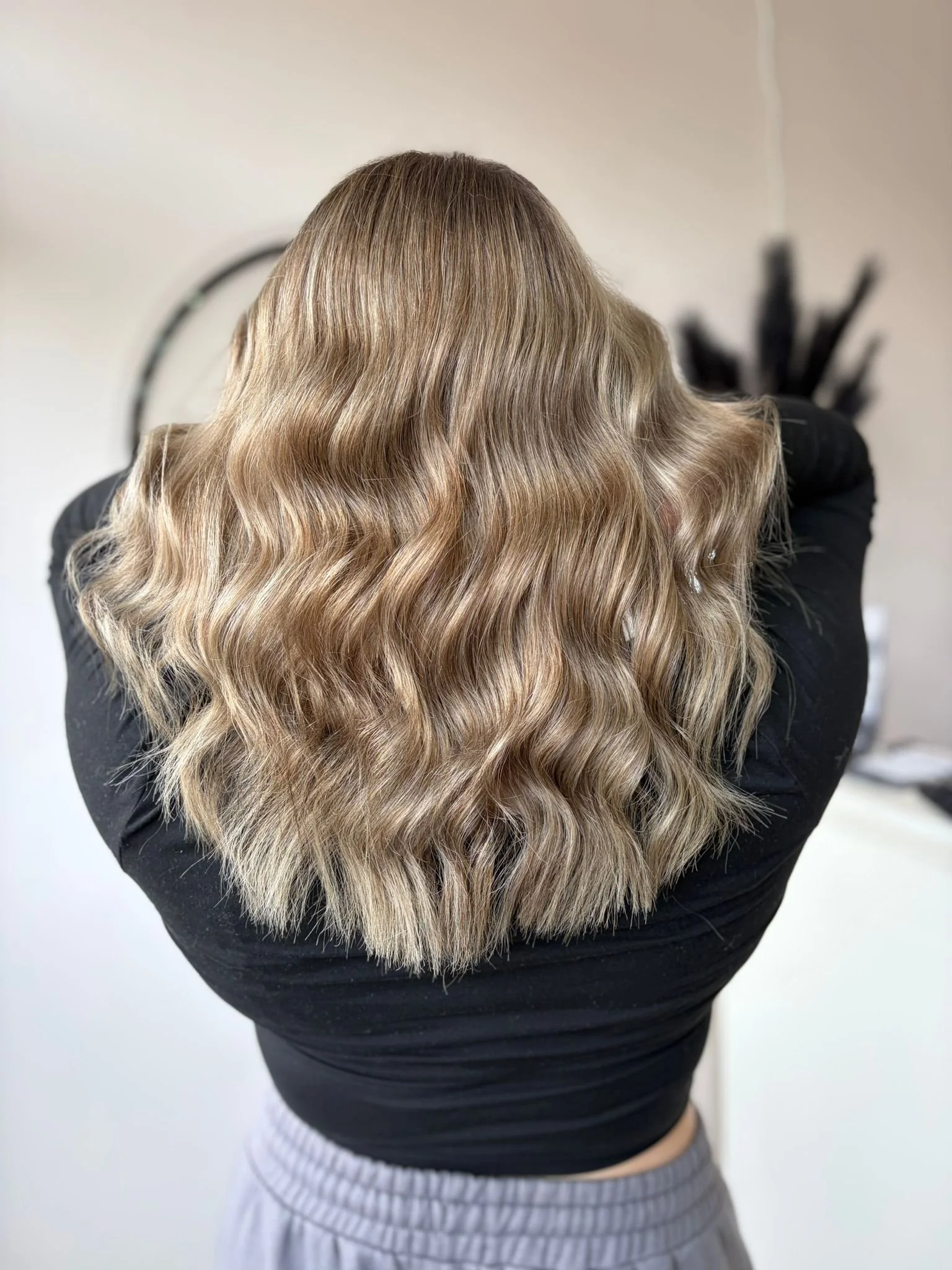 Back view of a person with shoulder-length wavy blonde hair, wearing a black top.