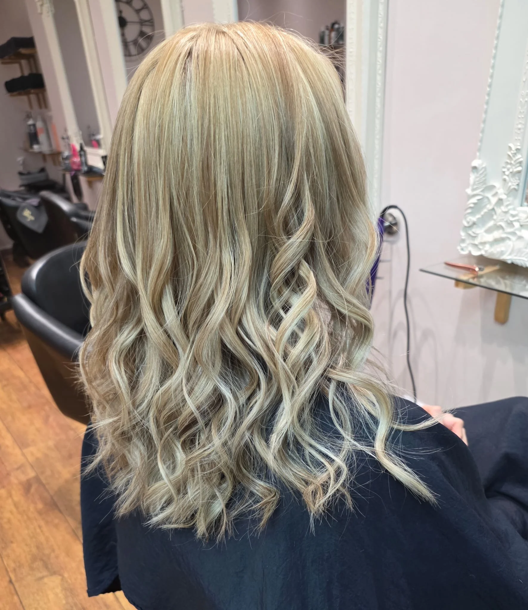 Blonde woman with shoulder-length curly hair sitting in a hair salon.