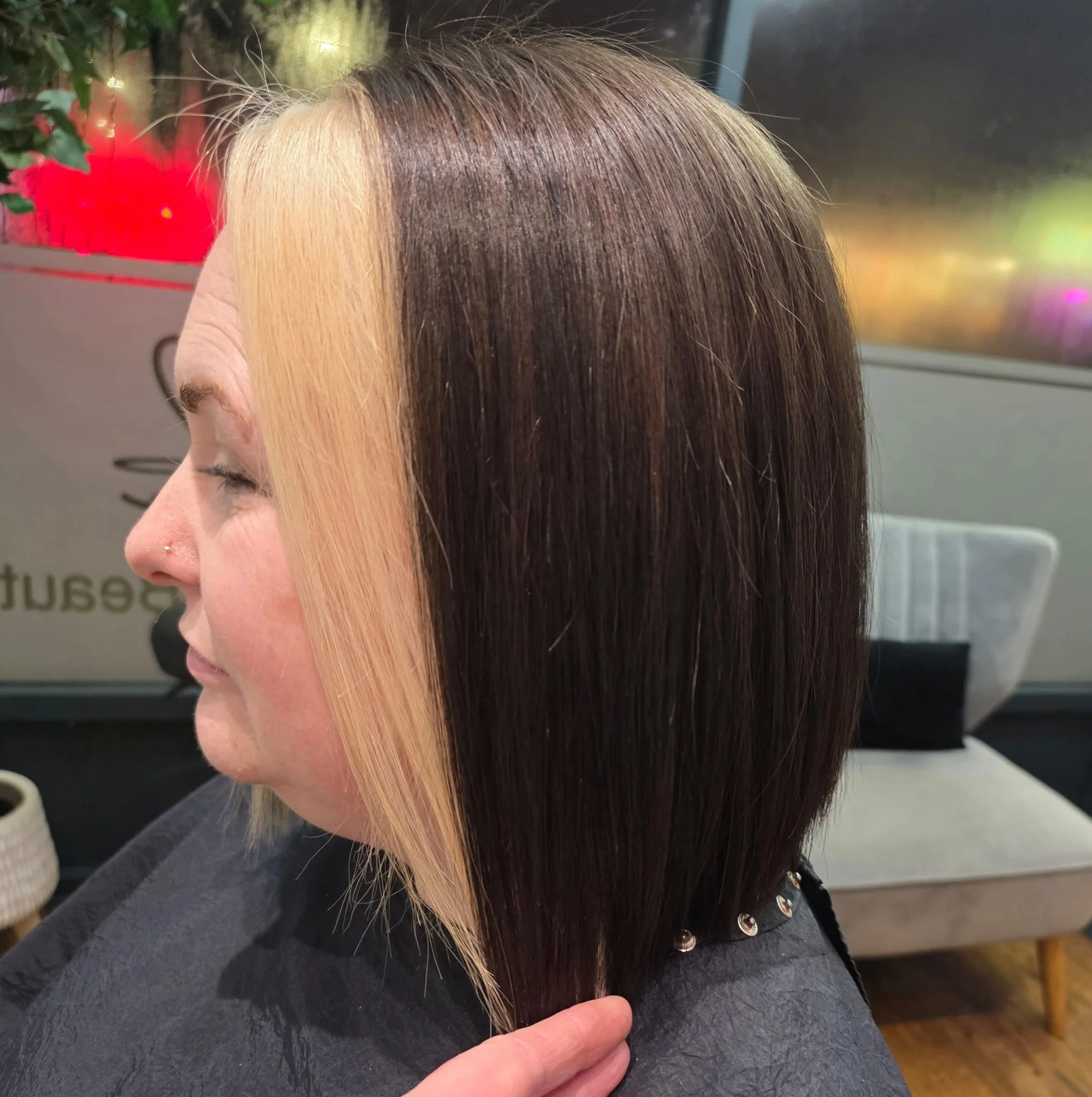 Side view of a woman with half her hair dyed blonde and the other half dark brown, sitting in a salon chair.