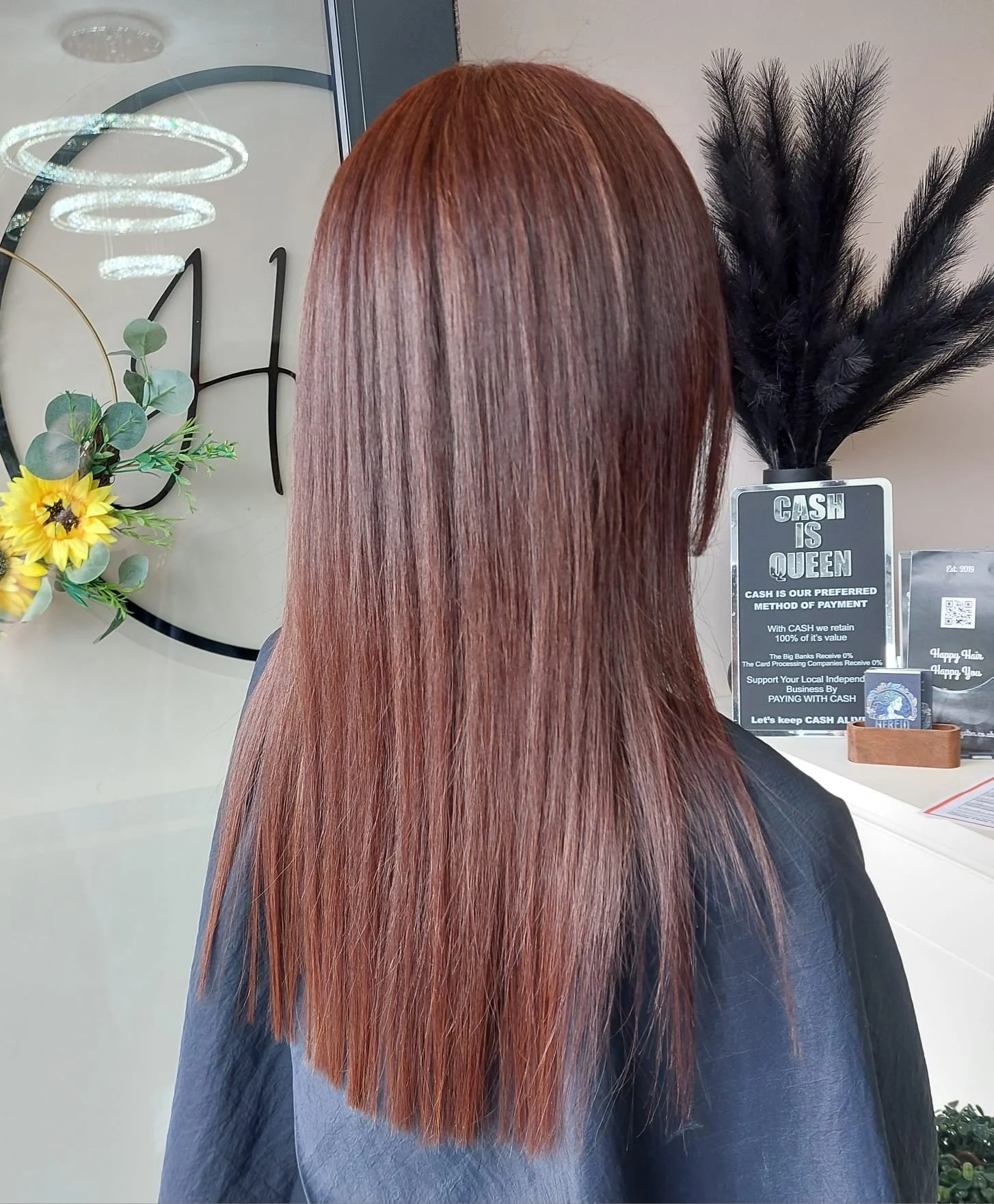 Back view of a woman with straight, shiny, reddish-brown hair in a salon.