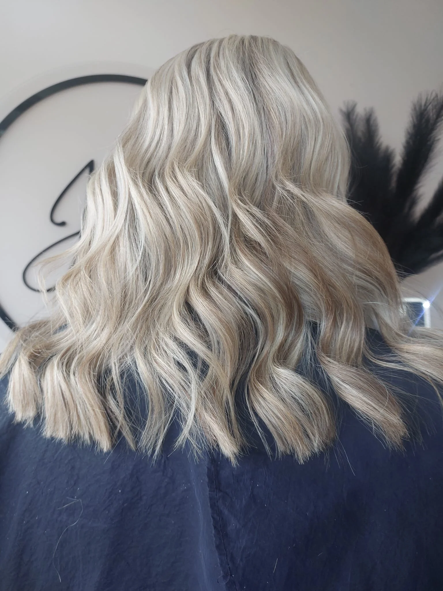Back of a woman's head showing long, wavy, blonde hair with subtle highlights.