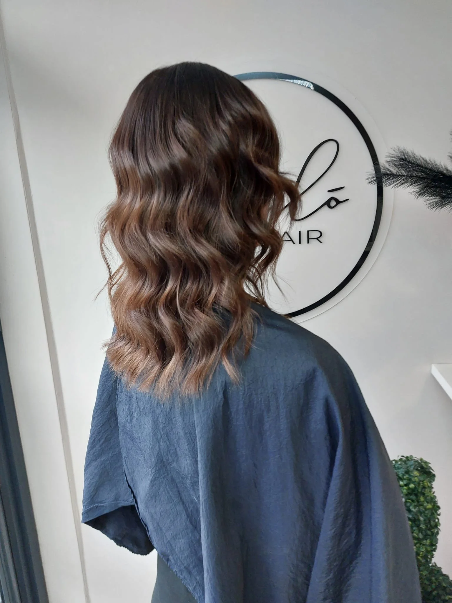 Side view of a woman with wavy, brown hair after a professional haircut and styling in a salon.