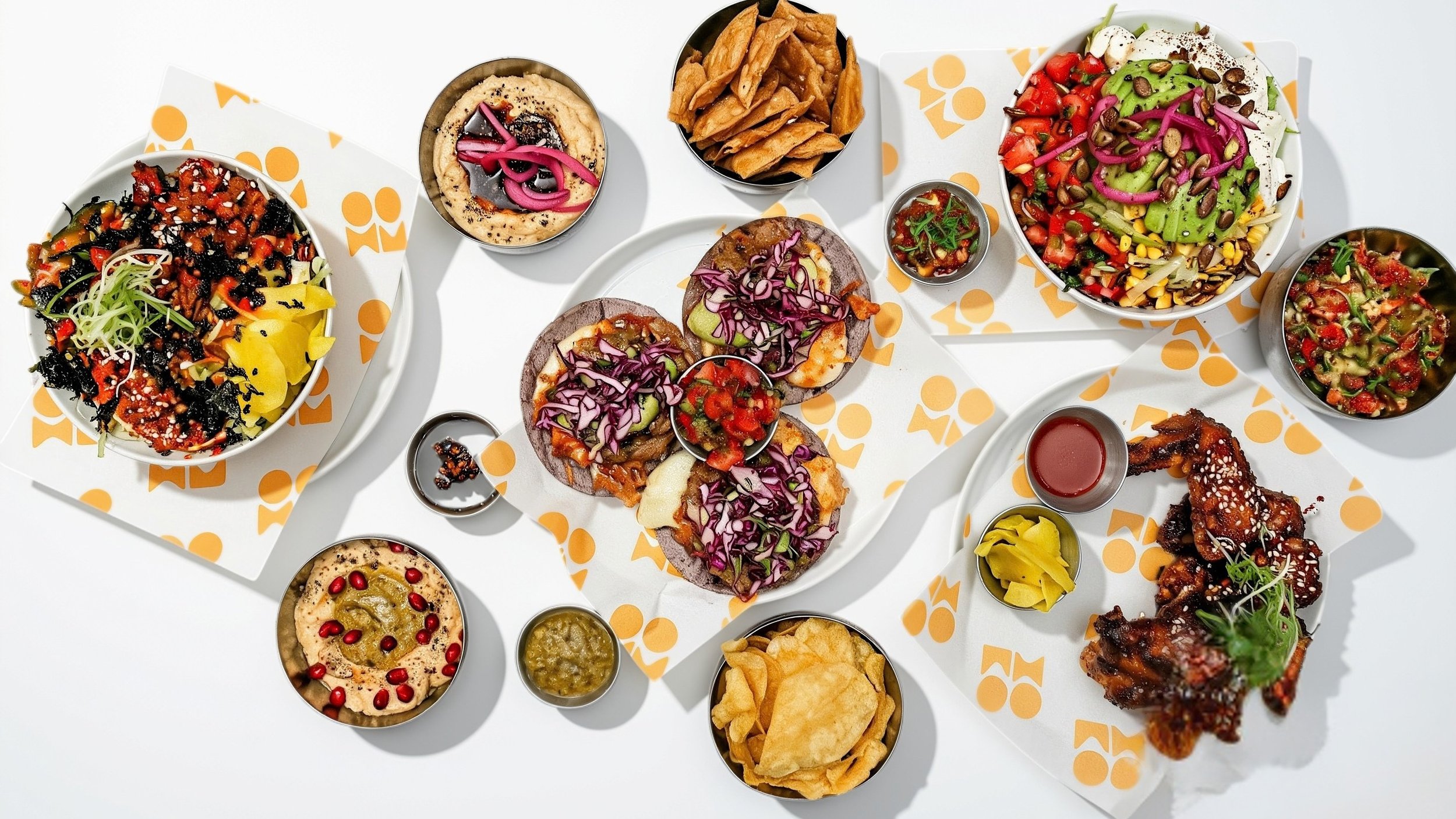 Assorted Mexican dishes including tacos, tortilla chips, salads, dips, and sauces on white table.